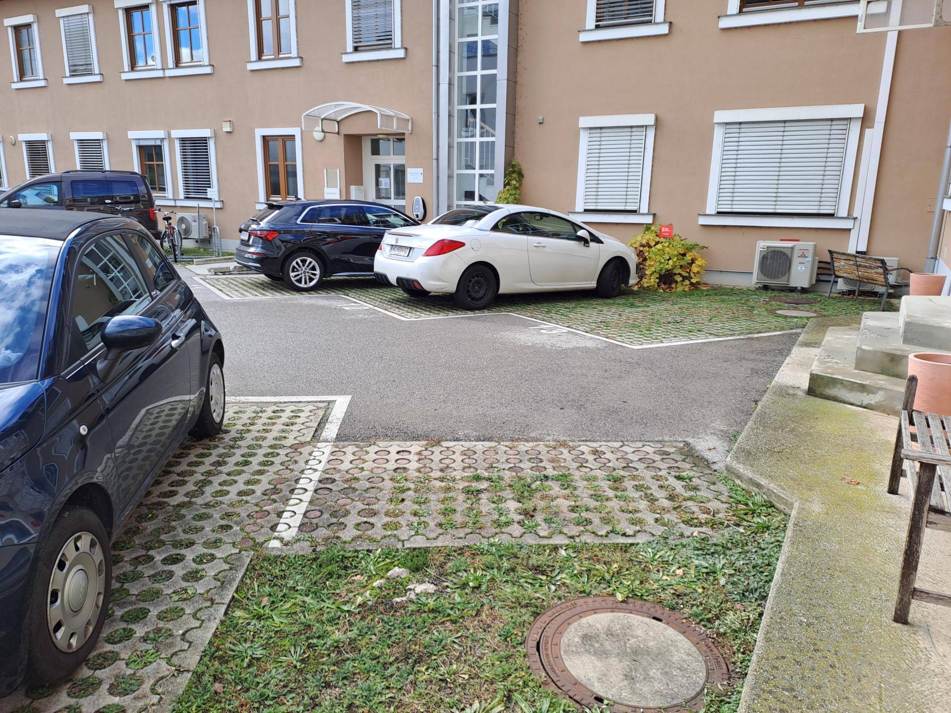 Außenansicht des Gebäudes mit Parkplätzen, Autos und einem begrünten Bereich.