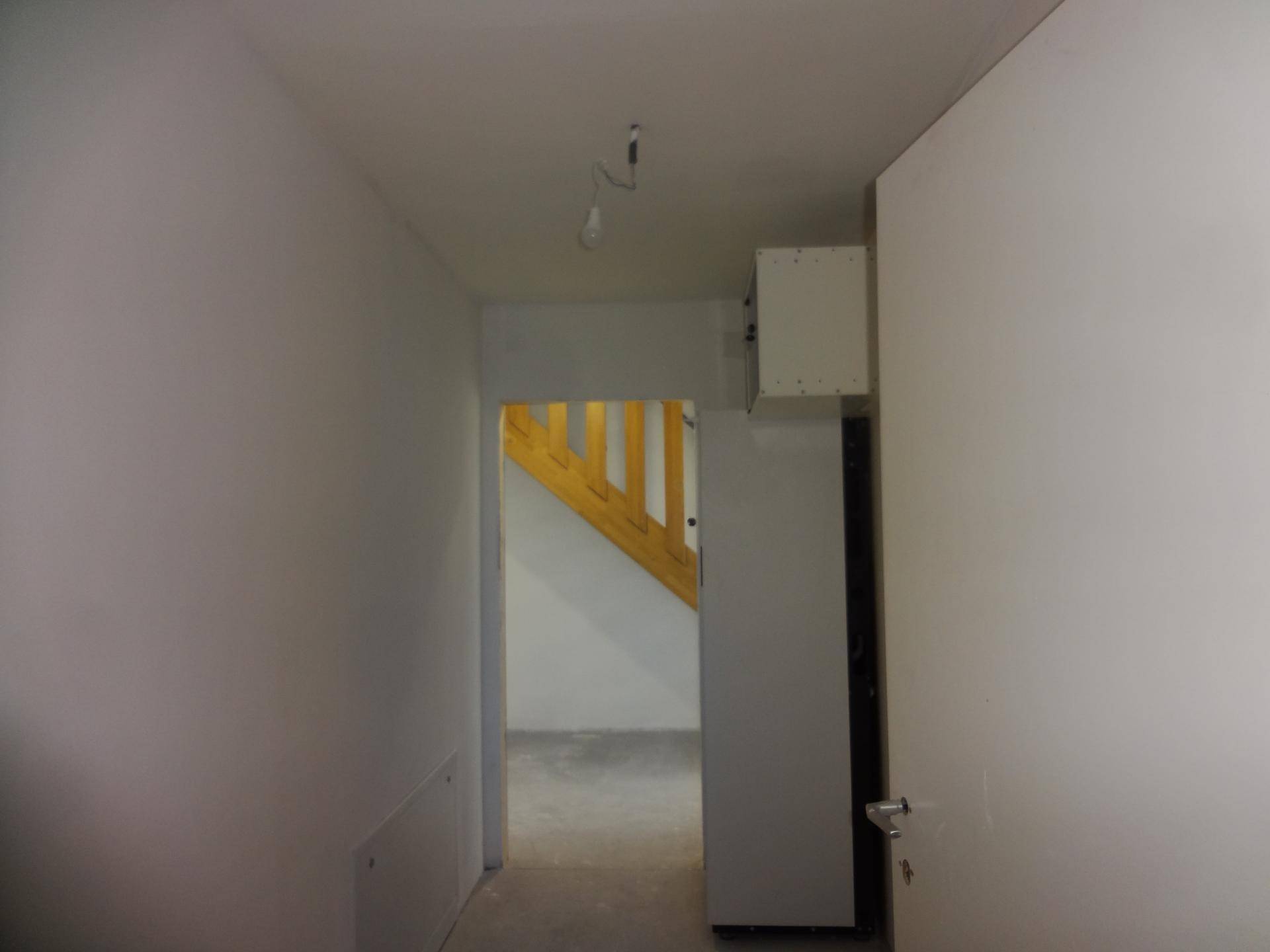 Unfertiger Flur mit weiß gestrichenen Wänden und Blick auf eine Holztreppe.