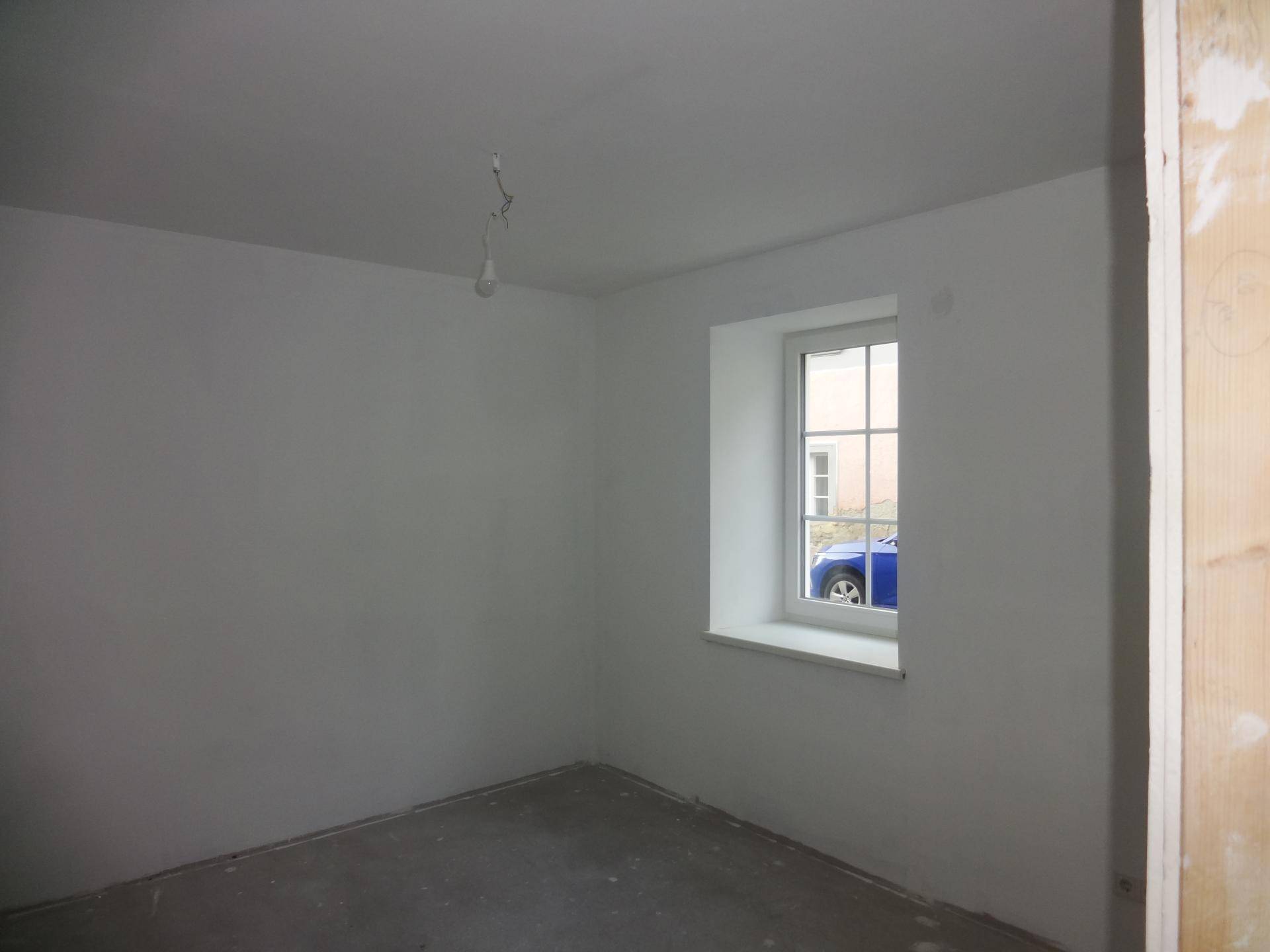 Unfertiger Raum mit einem Fenster und Betonboden, ideal für Schlafzimmer oder Büro.