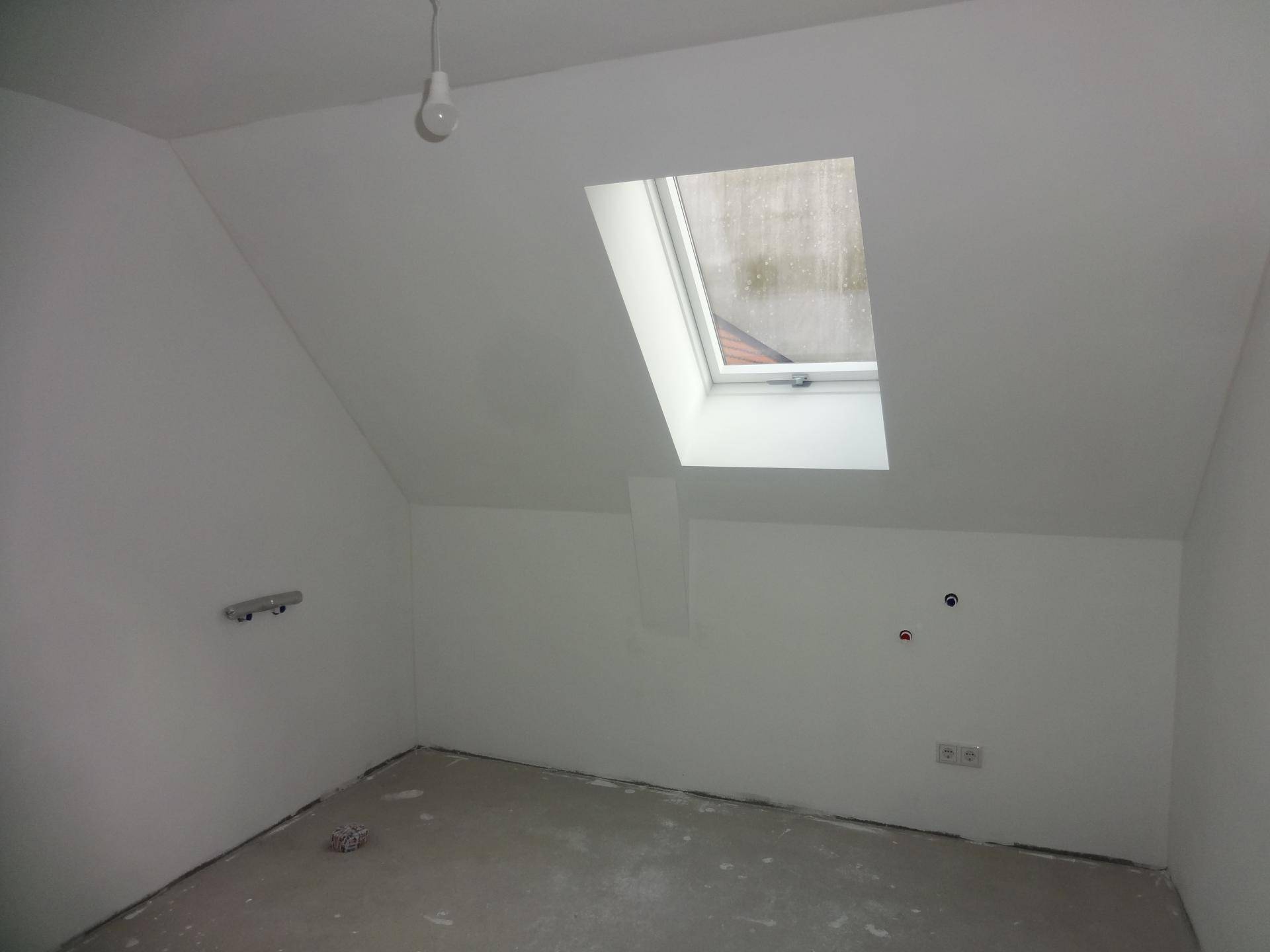 Unfertiger Raum im Dachgeschoss mit Schrägdach, Dachfenster und Betonboden.