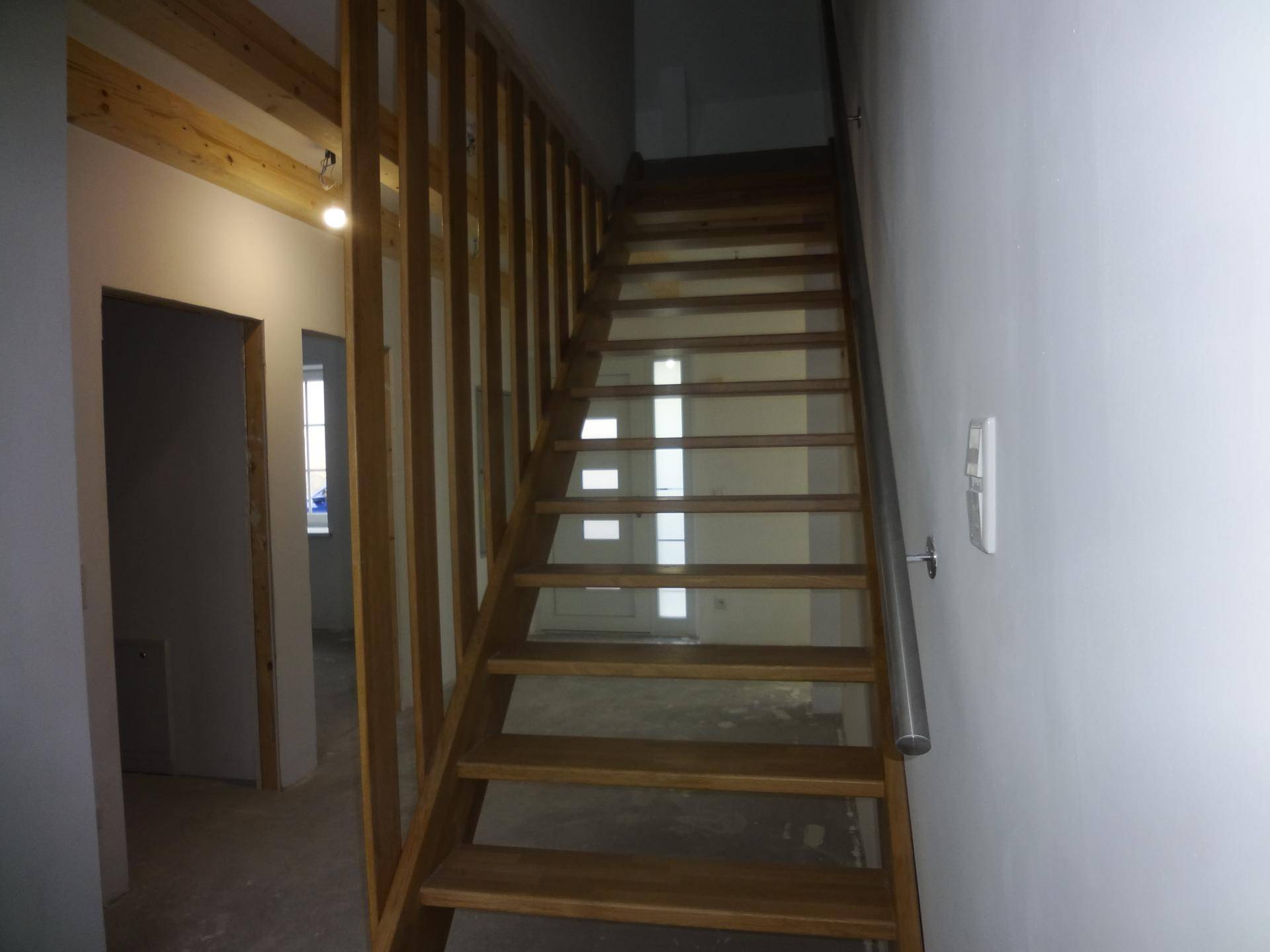 Holztreppe mit Geländer in einem unfertigen Innenbereich, führt in obere Etagen.