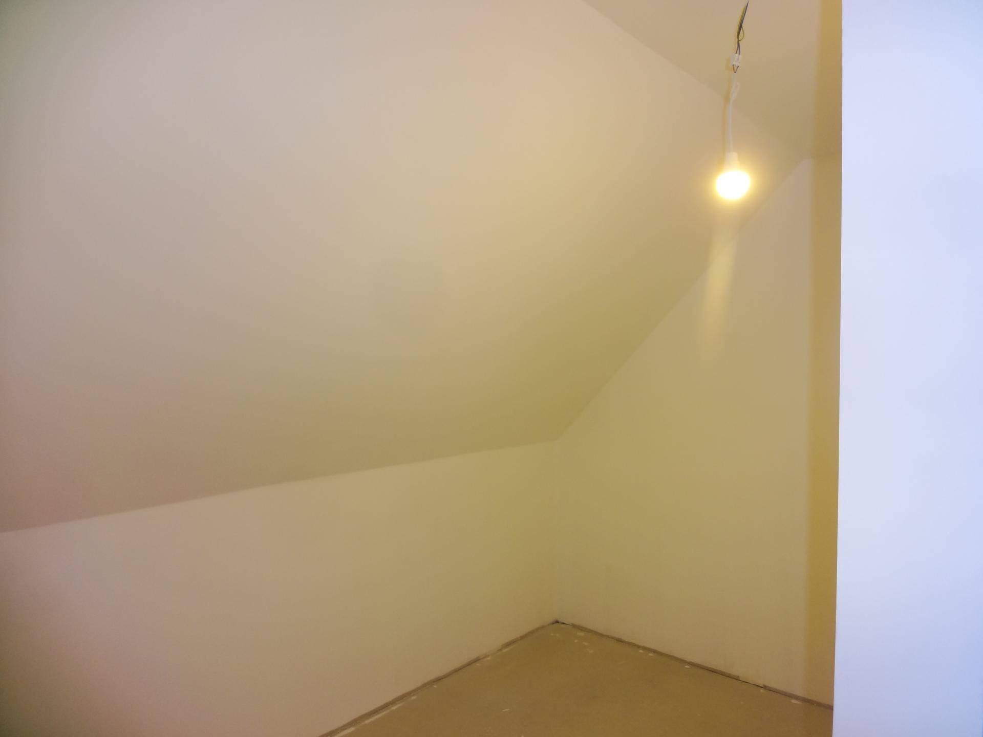 Kleiner, unfertiger Abstellraum im Dachgeschoss mit Schrägdach und einfacher Beleuchtung.