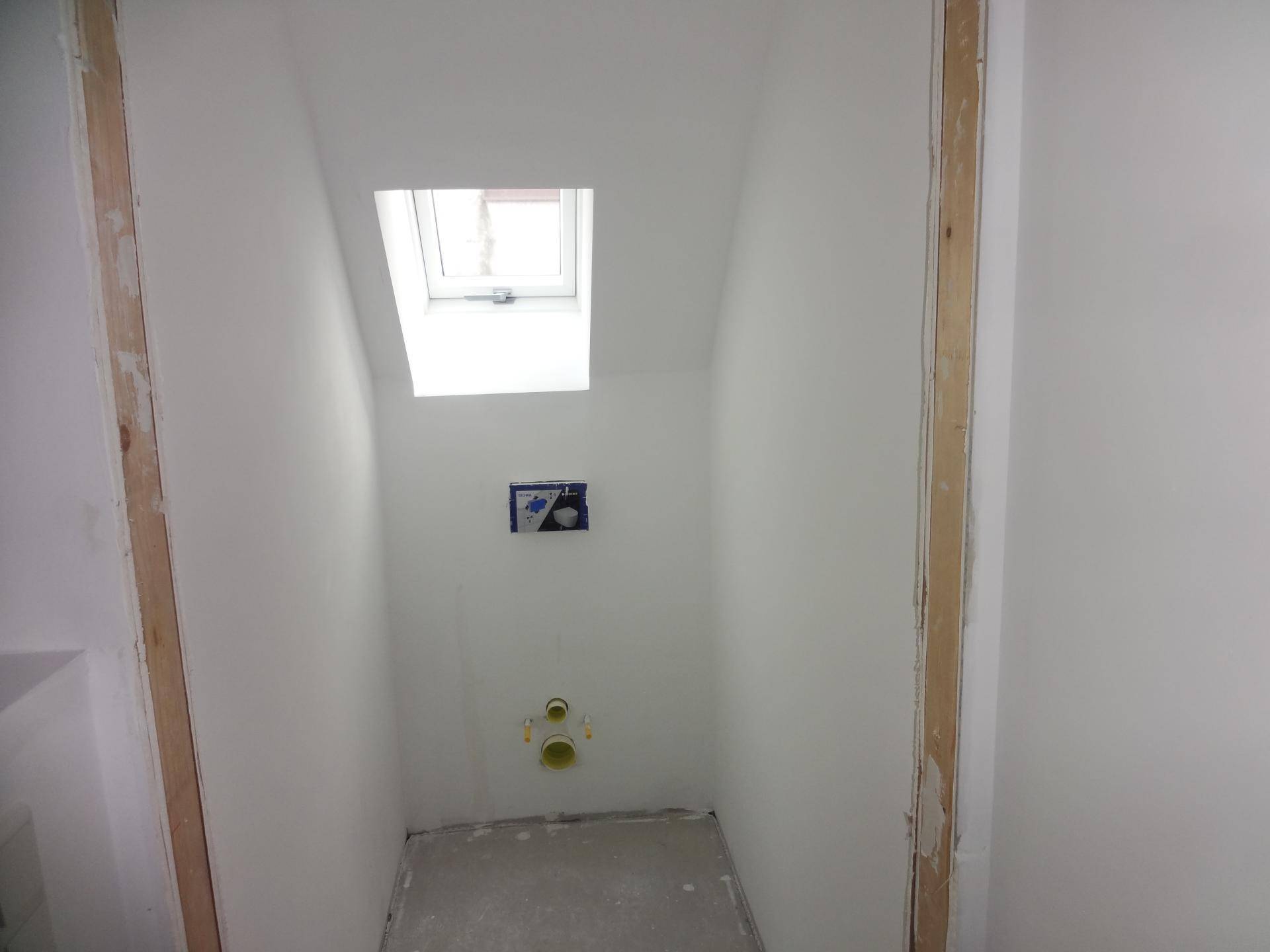 Kleiner, unfertiger Raum im Dachgeschoss mit Dachfenster und Anschlüssen für ein WC.