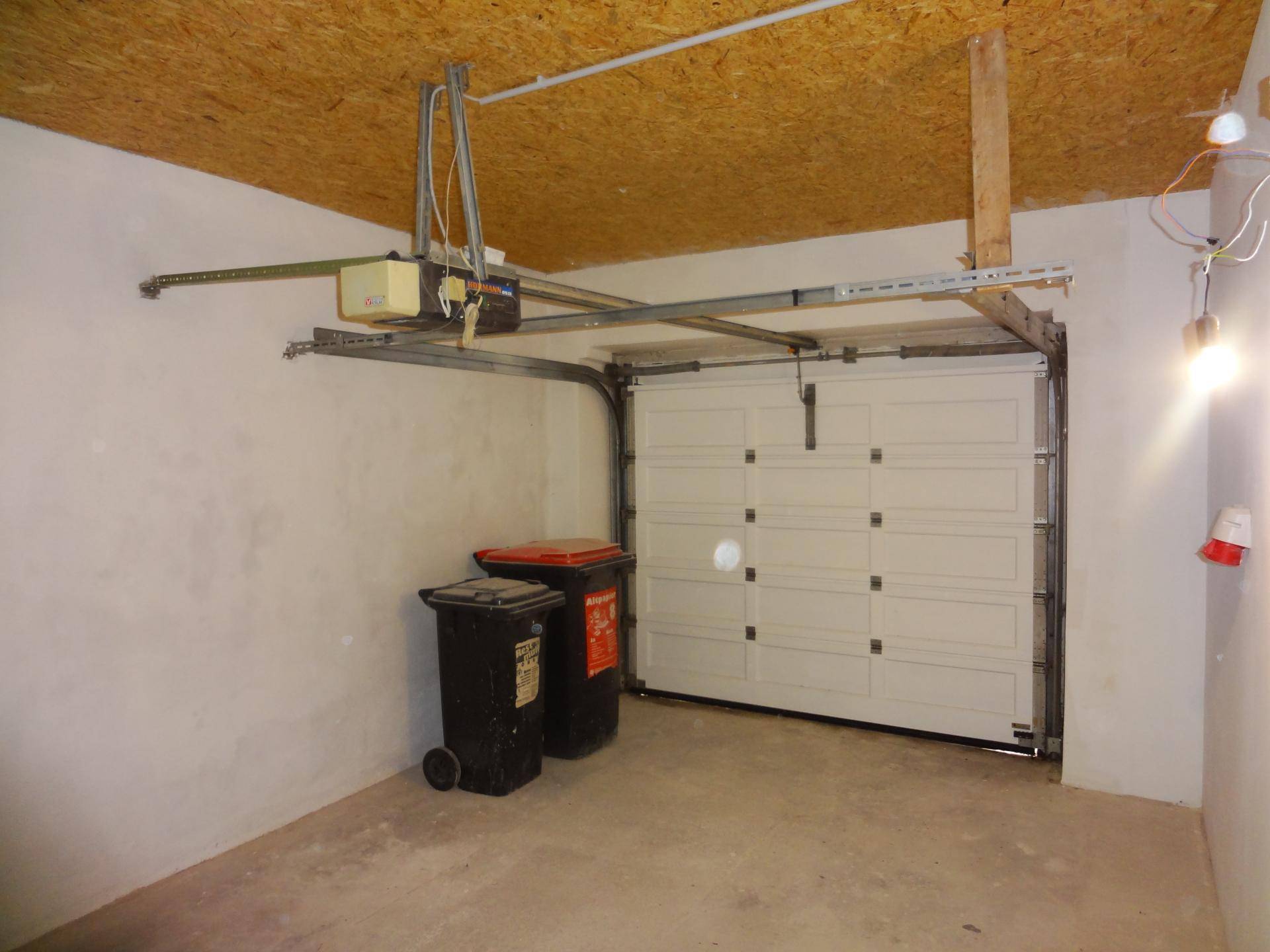 Garage mit automatischem Torantrieb, Betonboden und Abfallbehältern.