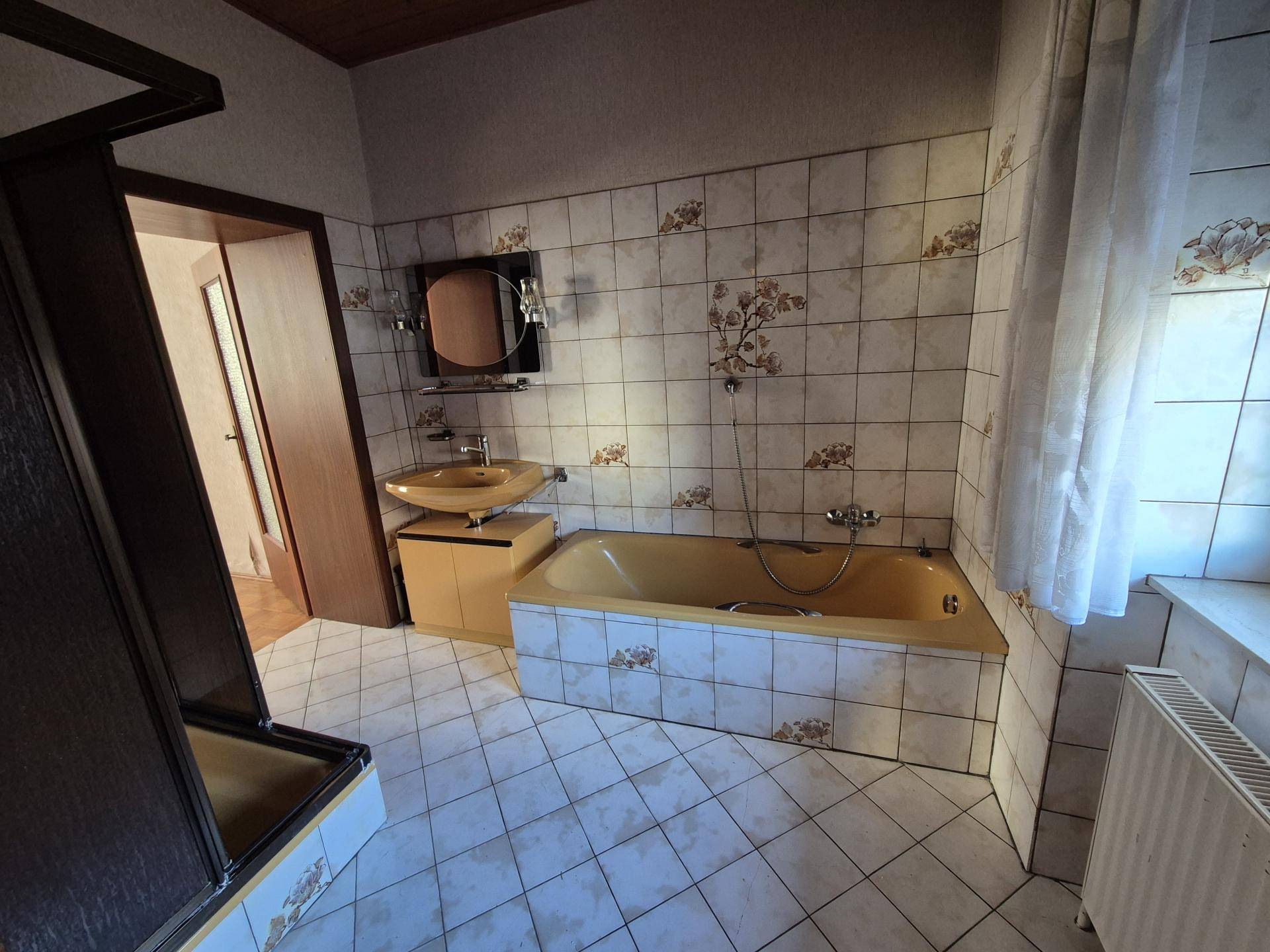 Badezimmer mit gelber Badewanne, passendem Waschbecken und gemusterten Wand- und Bodenfliesen.