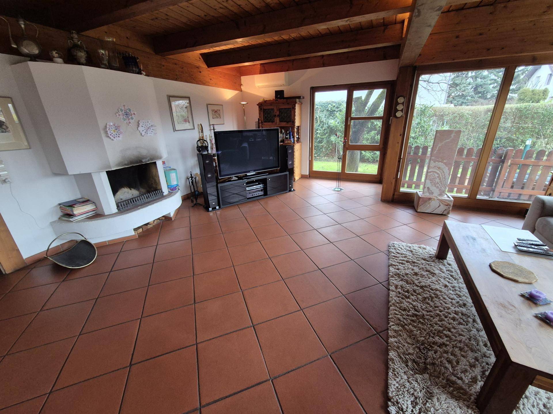Helles Wohnzimmer mit Kamin, Terrakottafliesen und großen Fenstern zum Garten.