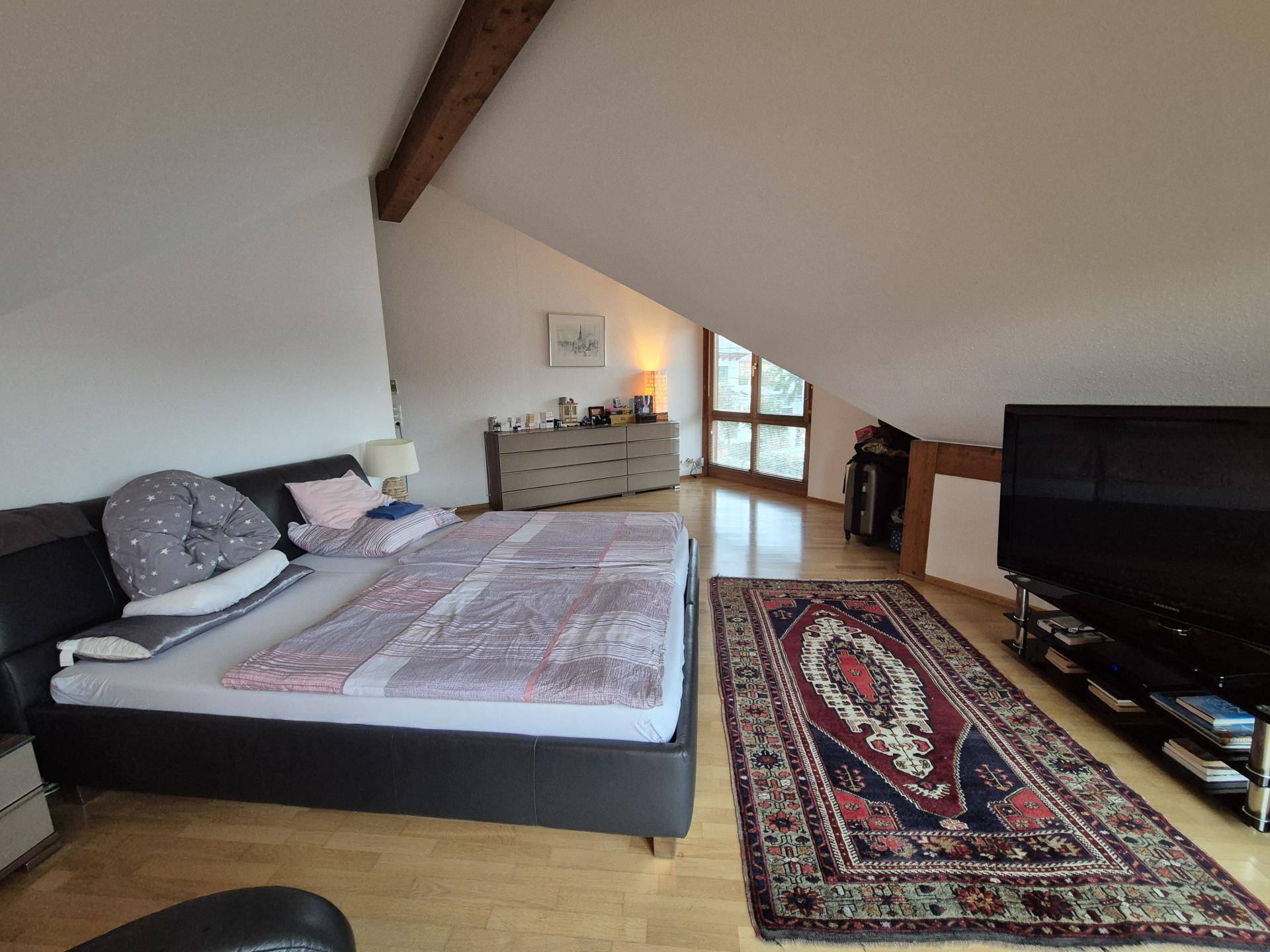 Geräumiges Schlafzimmer im Dachgeschoss mit Holzbalken, schrägen Wänden und Holzboden.