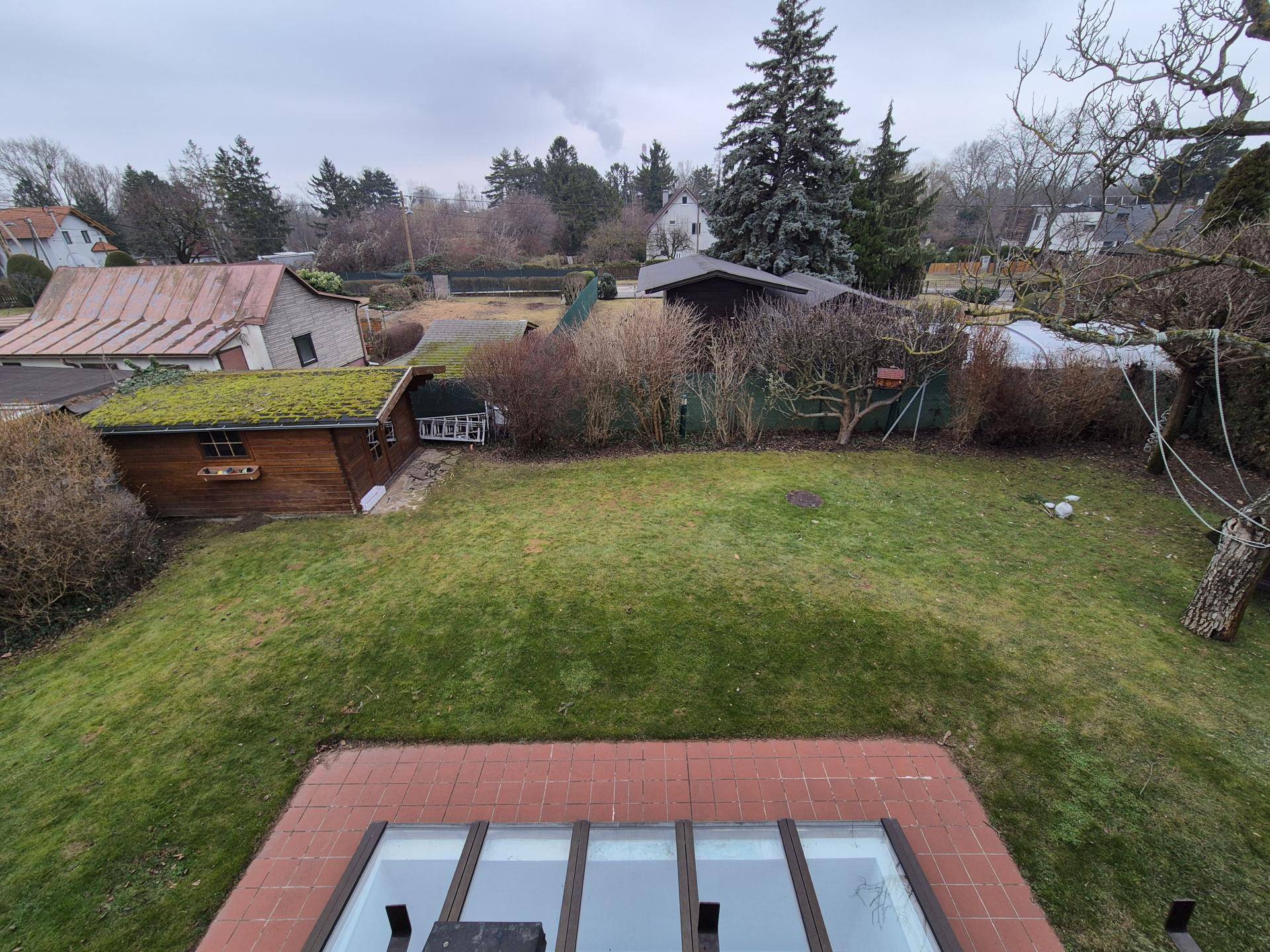 Weitläufiger Blick über den Garten mit Gartenhaus und umliegender Landschaft.