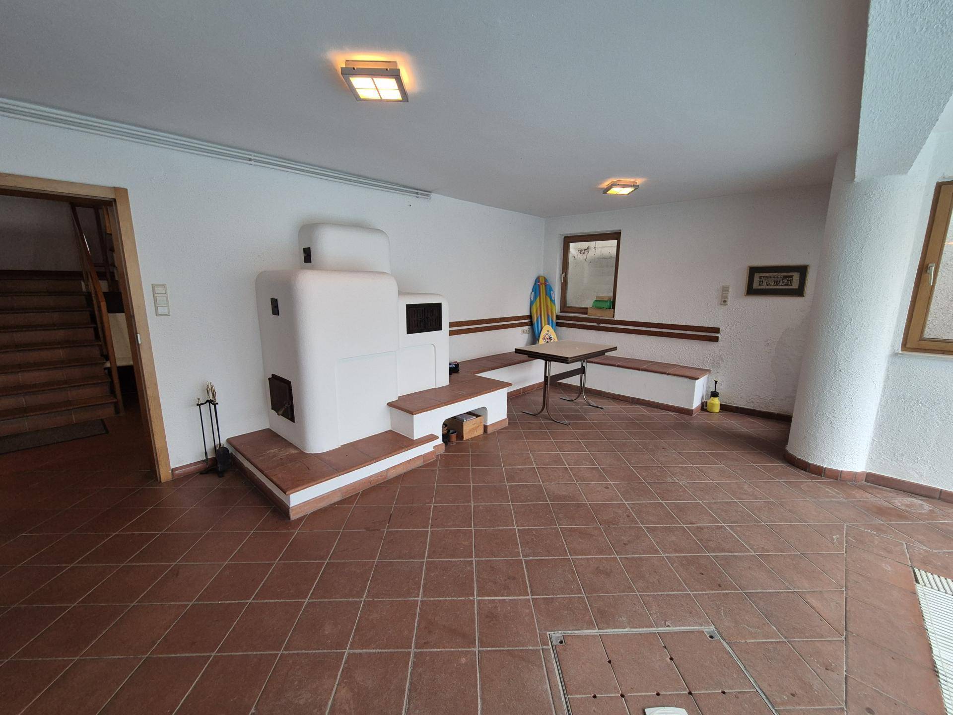 Geräumiger Wellnessbereich mit Kachelofen, Sitzgelegenheiten und Zugang zum Innenpool.