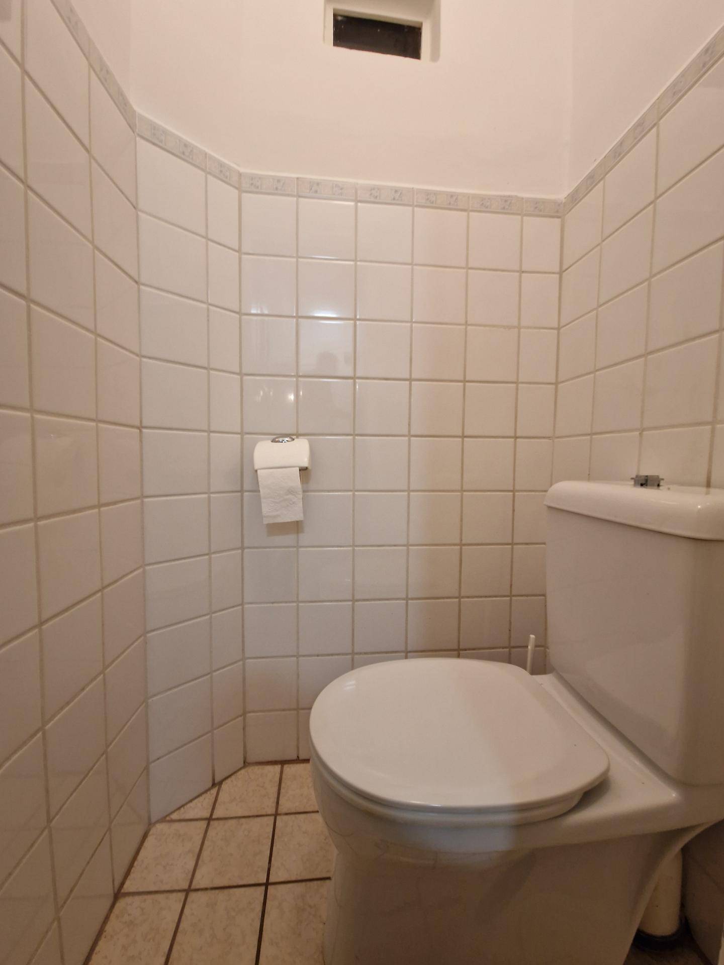 Separates WC mit weißen Fliesen und Standard-Toilette, sauber und funktional.