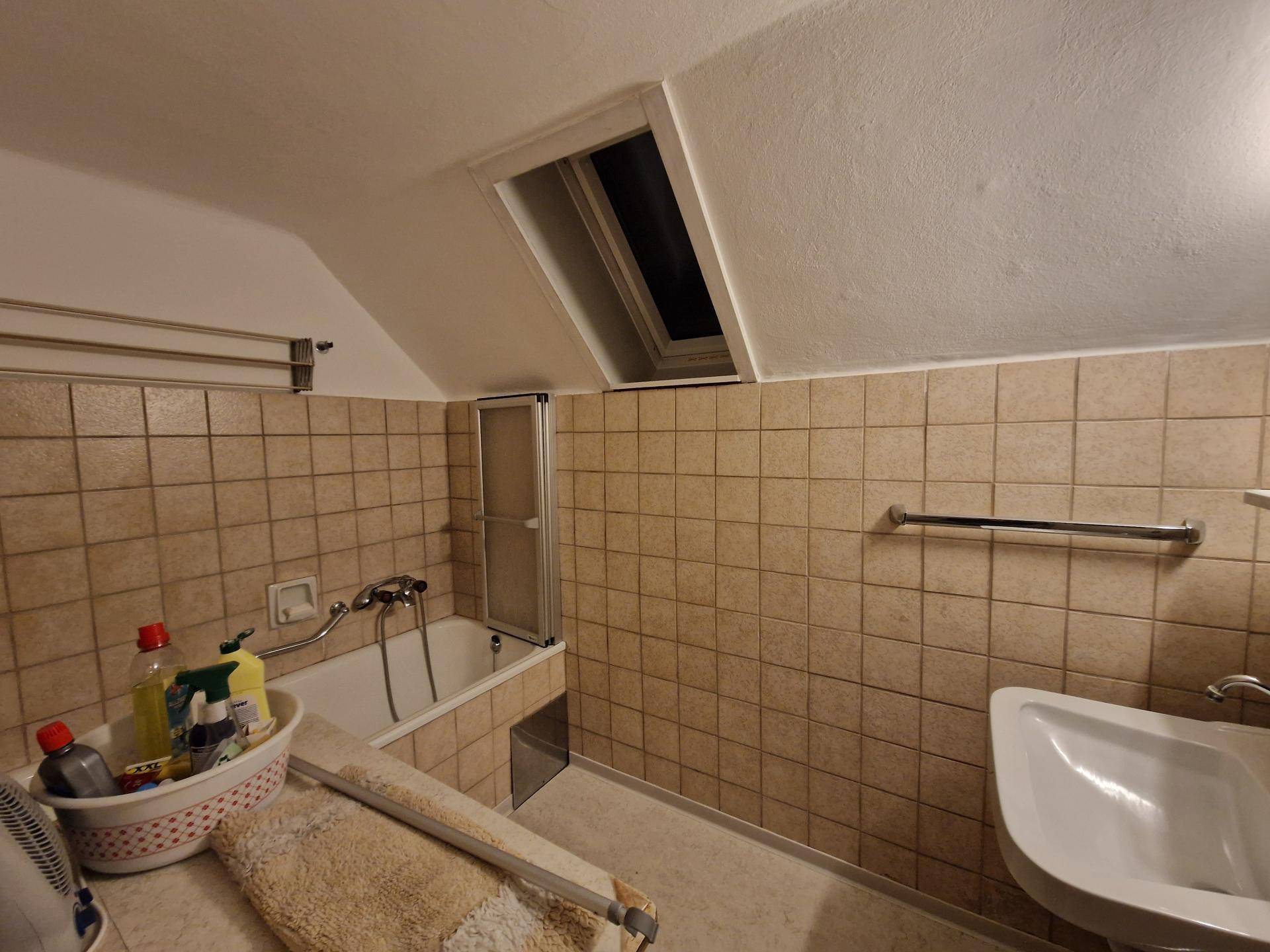Badezimmer im Dachgeschoss mit Badewanne, Waschbecken, Fliesen und Dachfenster.