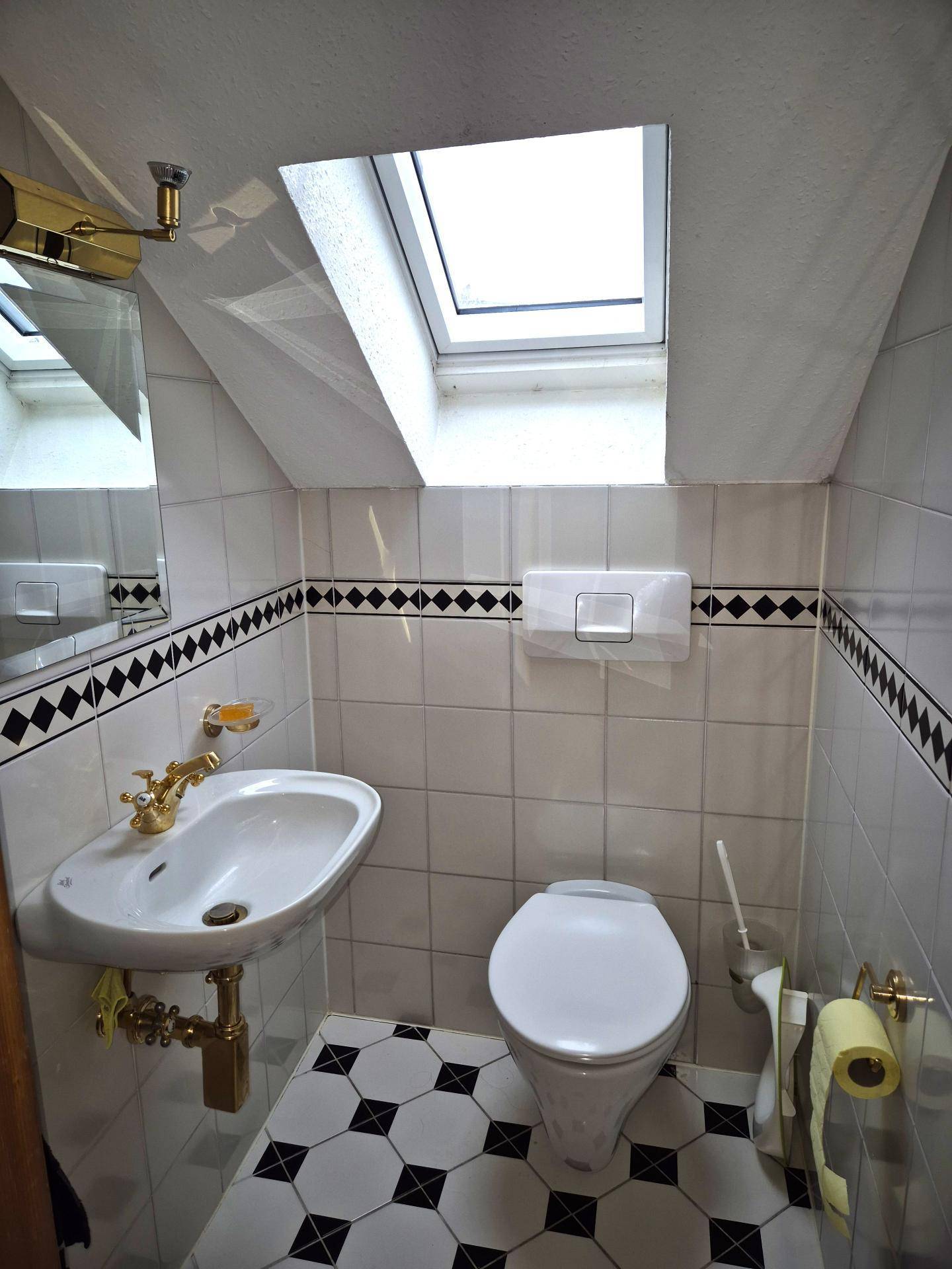 Kleines Gäste-WC mit Dachfenster, Waschbecken und schwarz-weißen Fliesen.