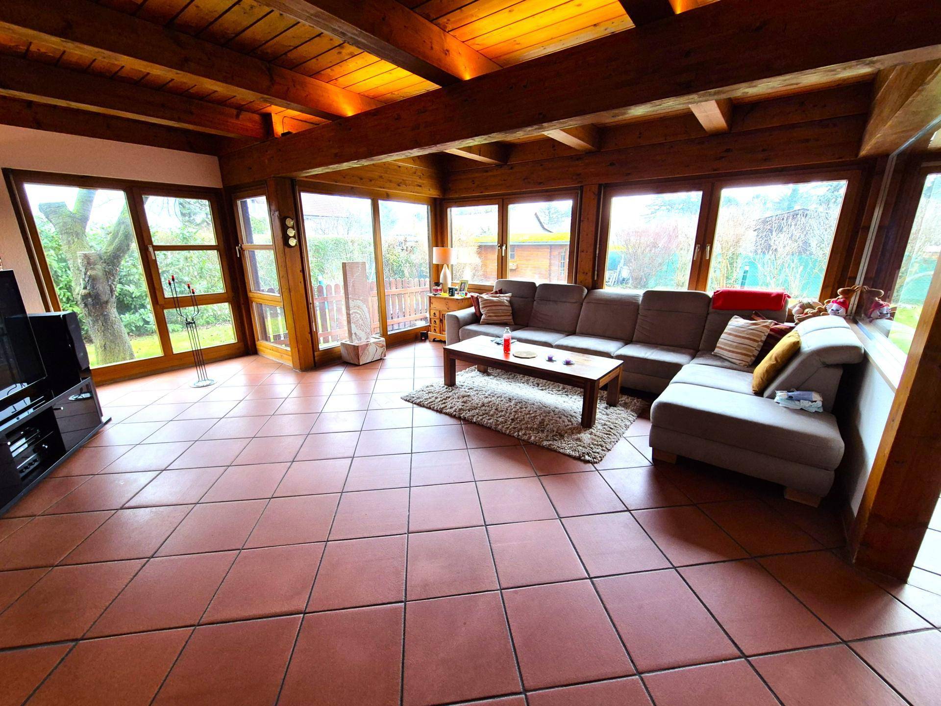 Geräumiges Wohnzimmer mit Holzbalkendecke, großen Fenstern und Terrakottaboden.