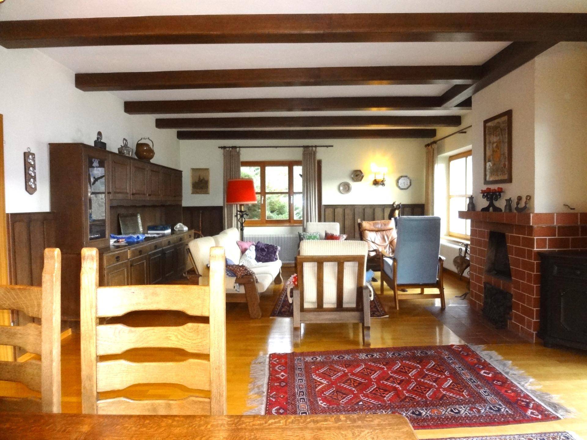 Gemütliches Wohnzimmer mit Holzbalken an der Decke, Parkettboden und einem traditionellen Kamin.