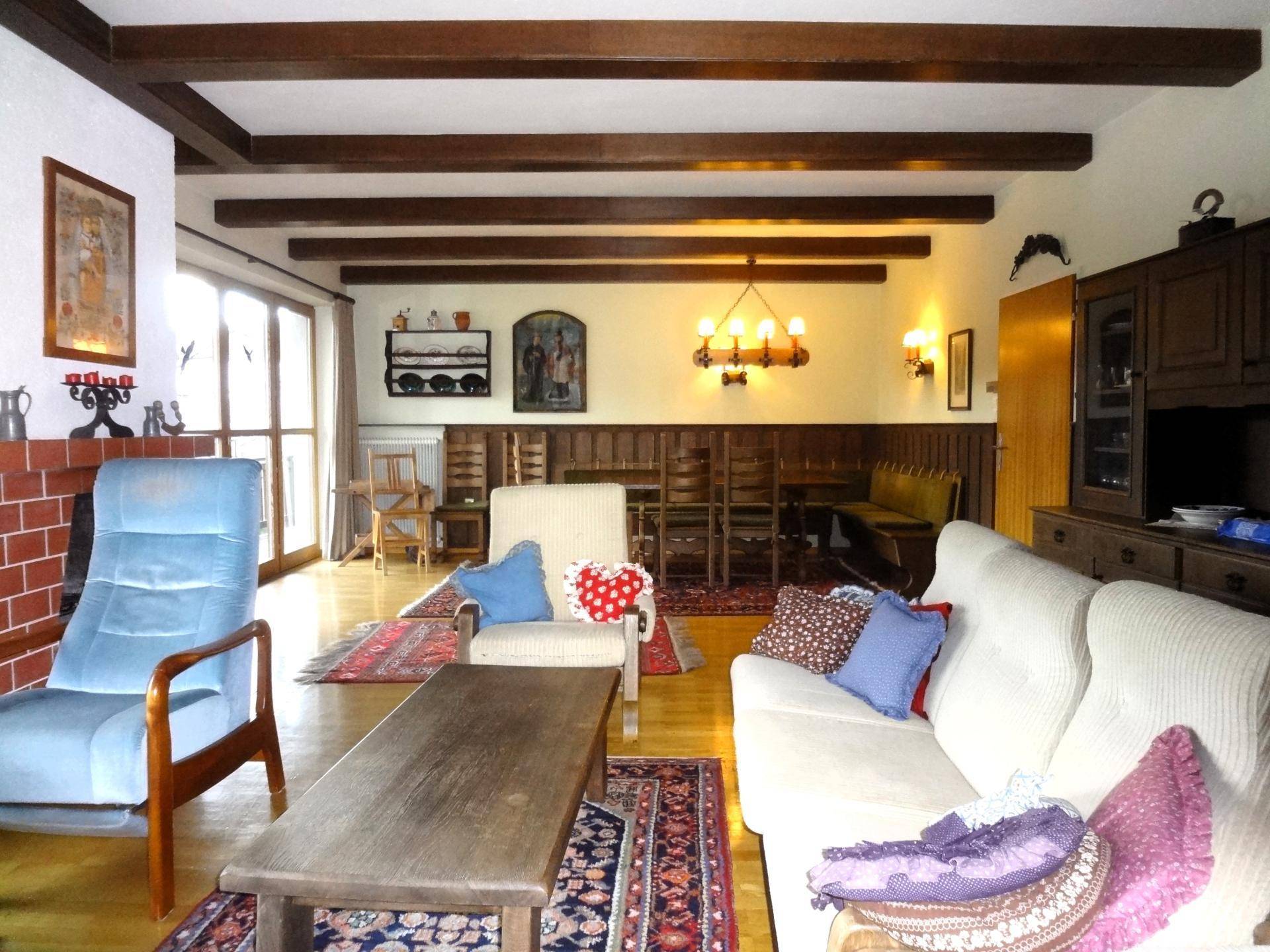 Geräumiges Wohnzimmer mit sichtbaren Holzbalken, Parkettboden und Zugang zu einem Außenbereich.