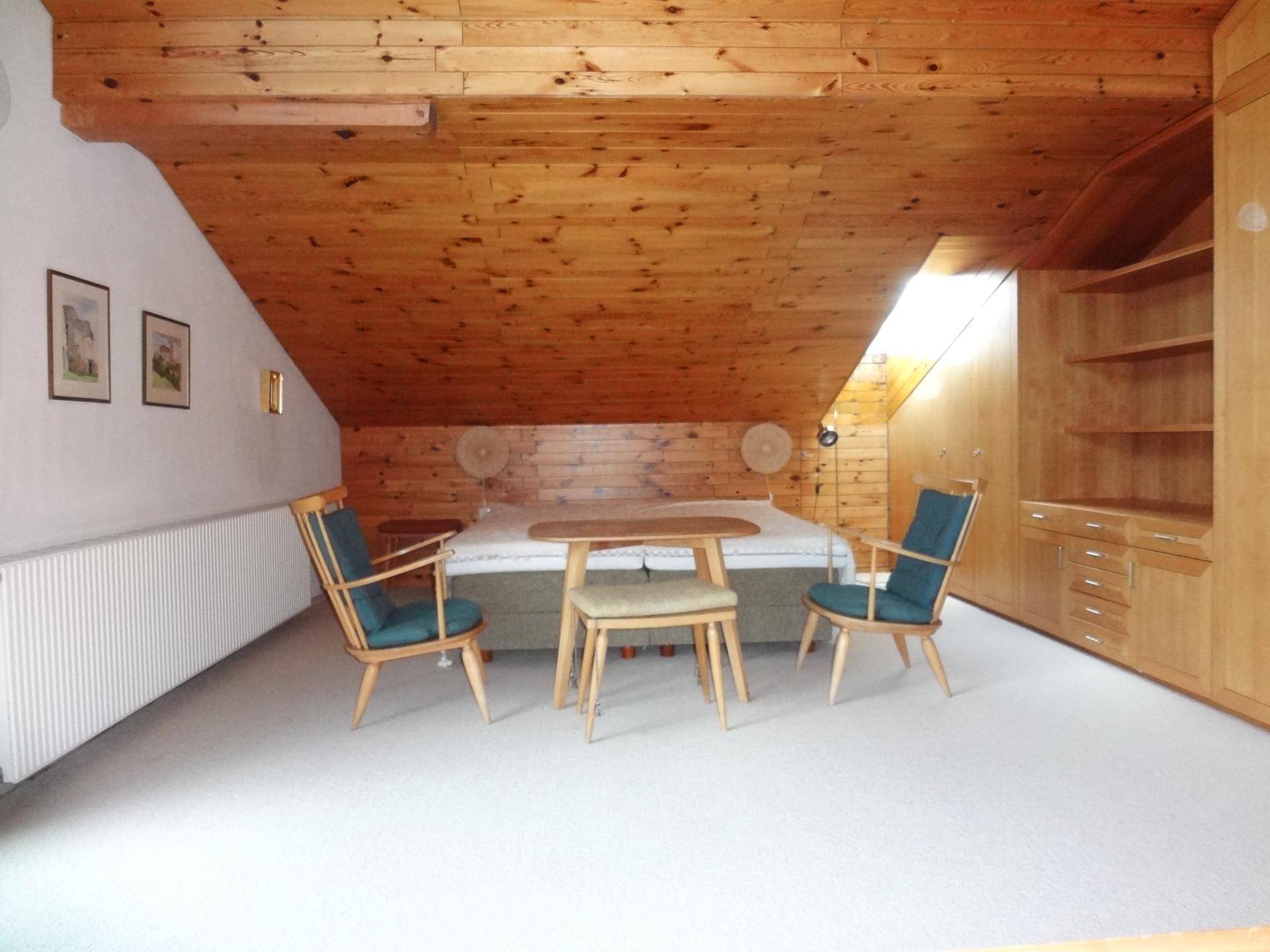 Gemütliches Schlafzimmer im Dachgeschoss mit schräger Holzdecke und integrierten Holzmöbeln.
