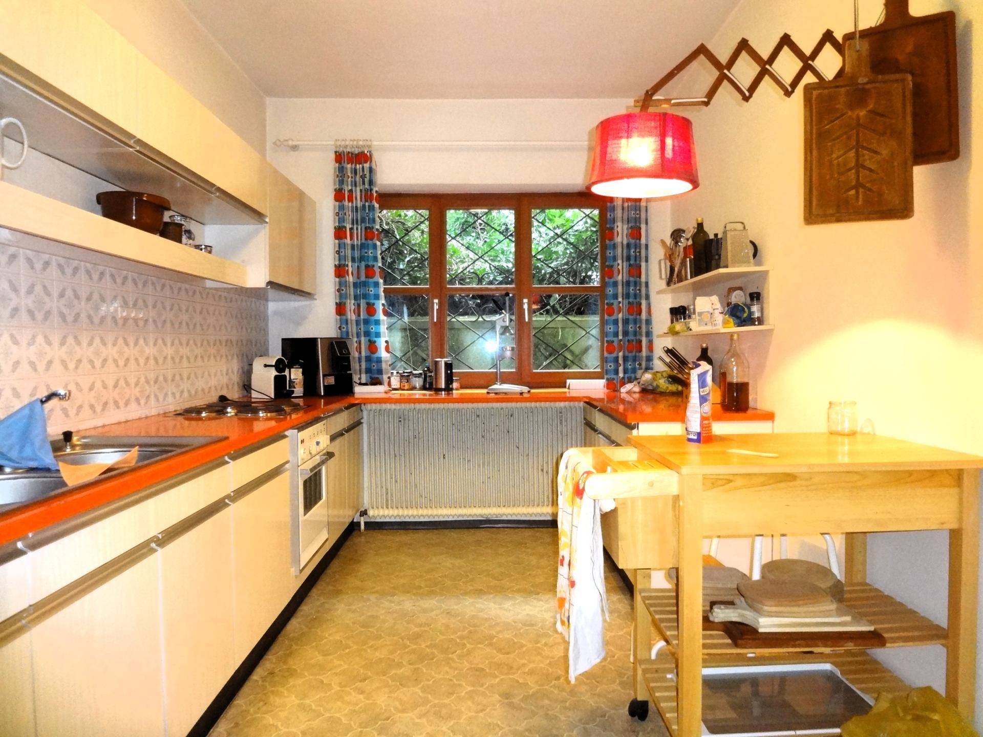 Küche im 80er-Jahre-Stil mit orangefarbenen Arbeitsplatten, weißen Schränken und einem Fenster mit Blick ins Grüne.