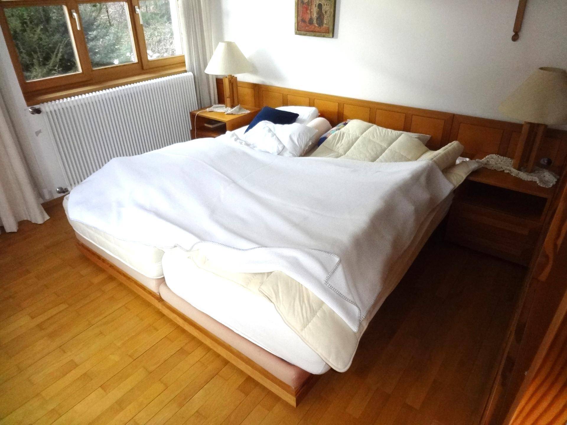 Schlafzimmer mit Doppelbett, Holzfußboden und einem Fenster, das viel Tageslicht hereinlässt.