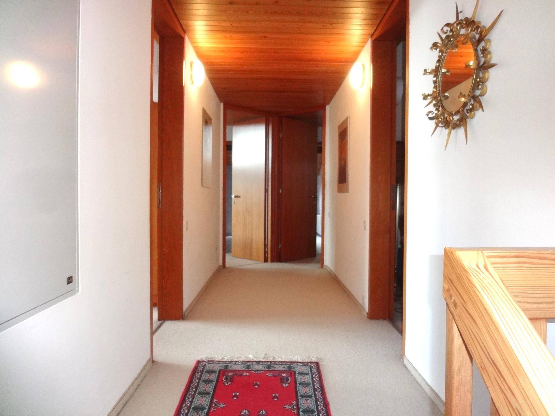 Heller Flur mit Holzdecke, Teppichboden und dekorativem Spiegel an der Wand.