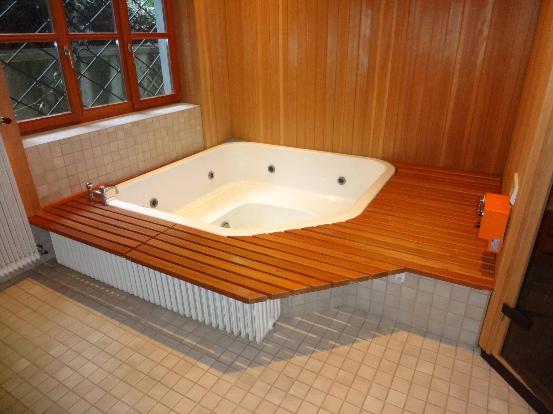 Badezimmer mit einem eingebauten Whirlpool, Holzverkleidung und Fliesenboden.