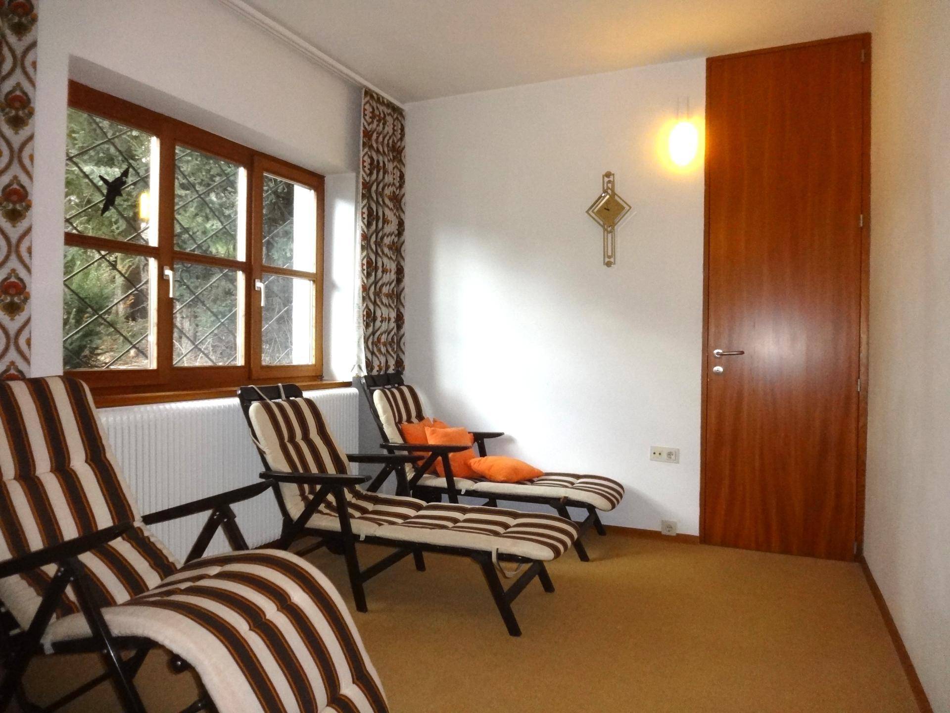 Entspannungsraum mit mehreren Liegestühlen, Teppichboden und einem Fenster mit Blick ins Grüne.