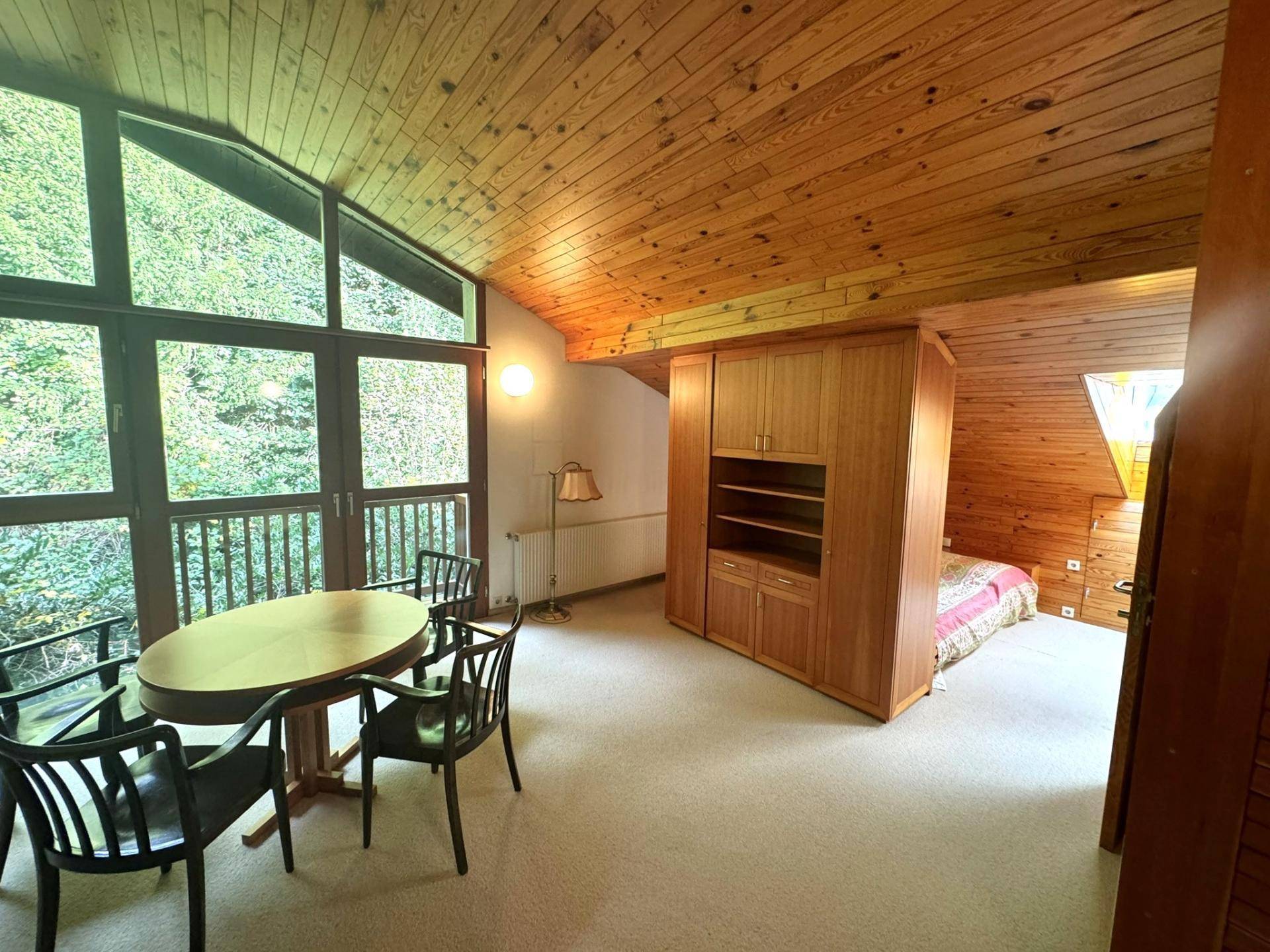 Heller Wohnbereich im Dachgeschoss mit schräger Holzdecke, großen Fenstern und Essbereich.