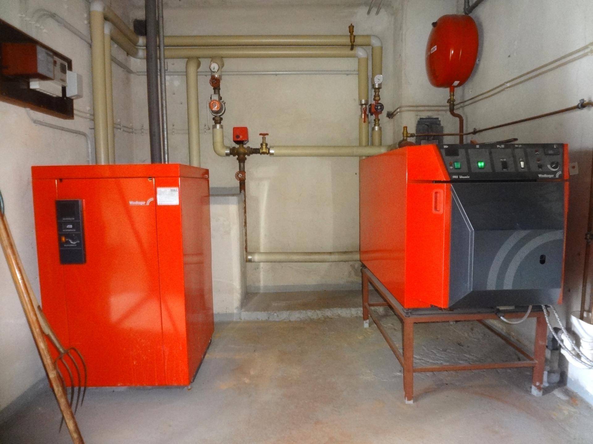 Heizungsraum mit zwei großen Heizkesseln und sichtbaren Rohrleitungen.