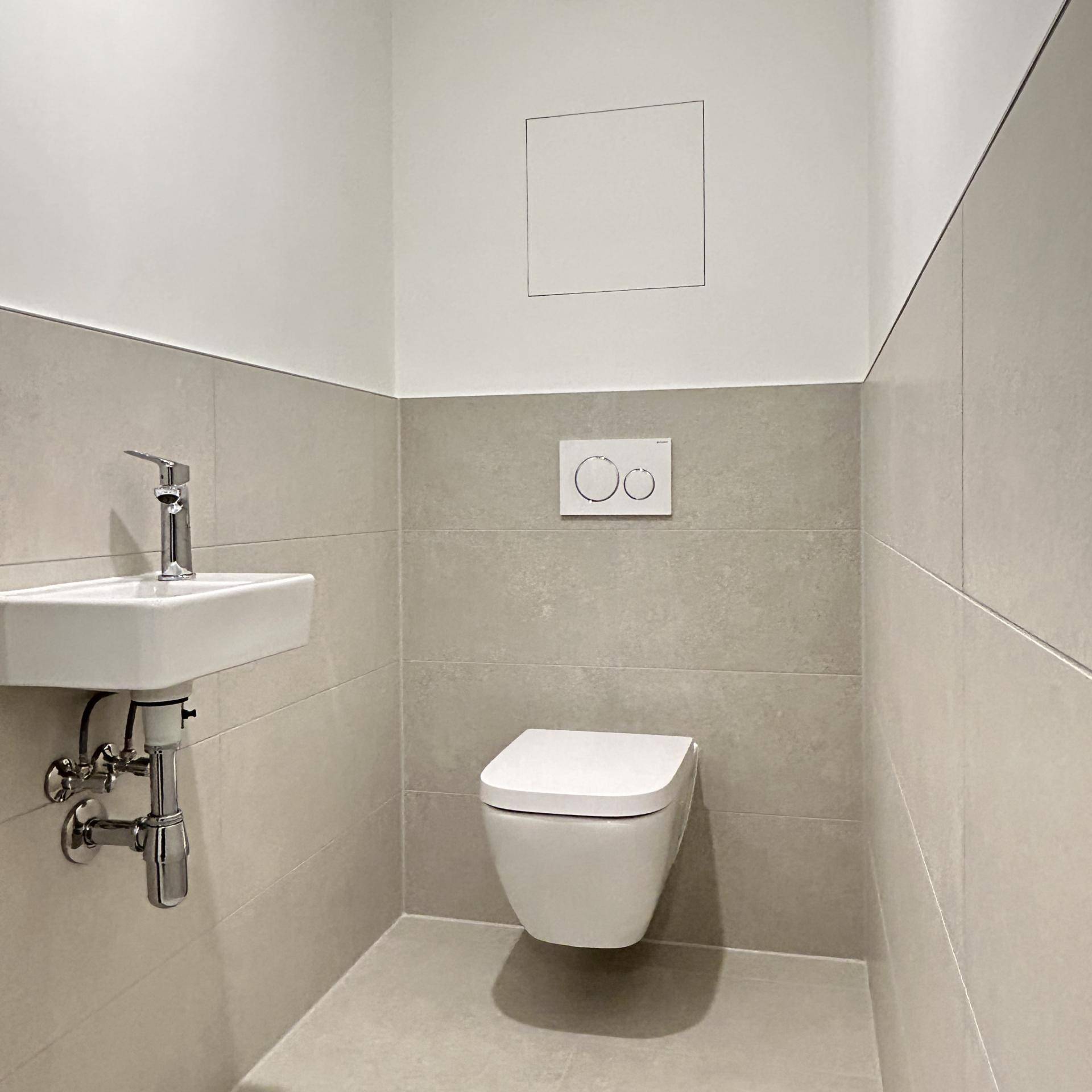 Kompaktes Gäste-WC mit wandhängender Toilette und kleinem Waschbecken, halbhoch gefliest.
