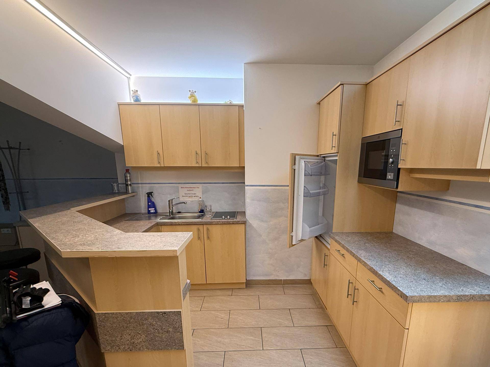 Funktionale Küchenzeile mit hellen Holzschränken, Mikrowelle und Kühlschrank, ideal für Pausen und kleine Mahlzeiten.
