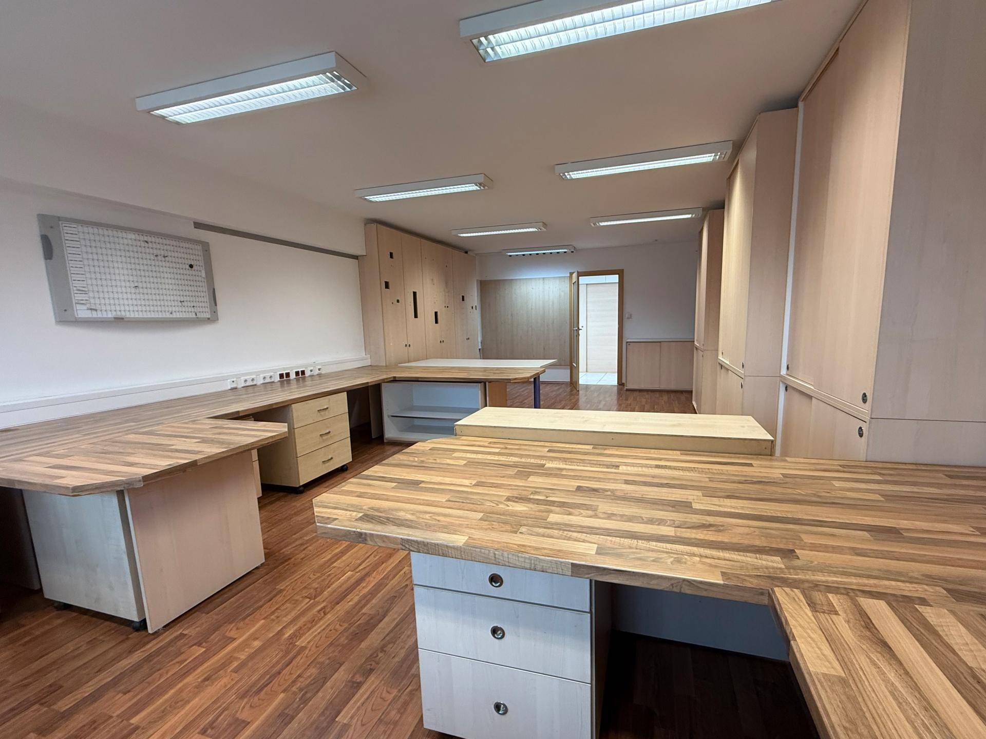 Geräumiges Büro mit mehreren Holzschreibtischen und integrierten Schränken, bietet viel Arbeitsfläche und Stauraum.