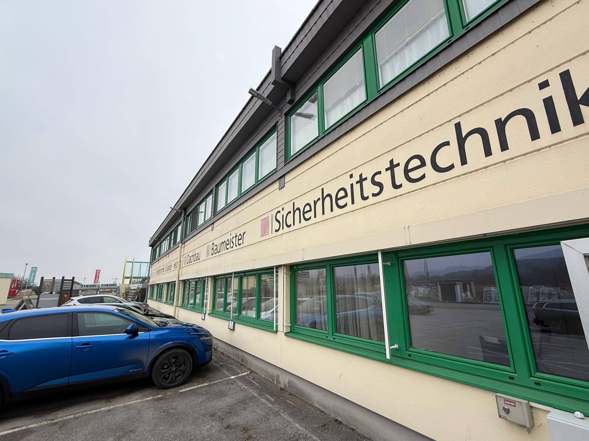 Seitenansicht eines modernen Geschäftsgebäudes mit grünen Fensterrahmen und Beschriftungen an der Fassade.