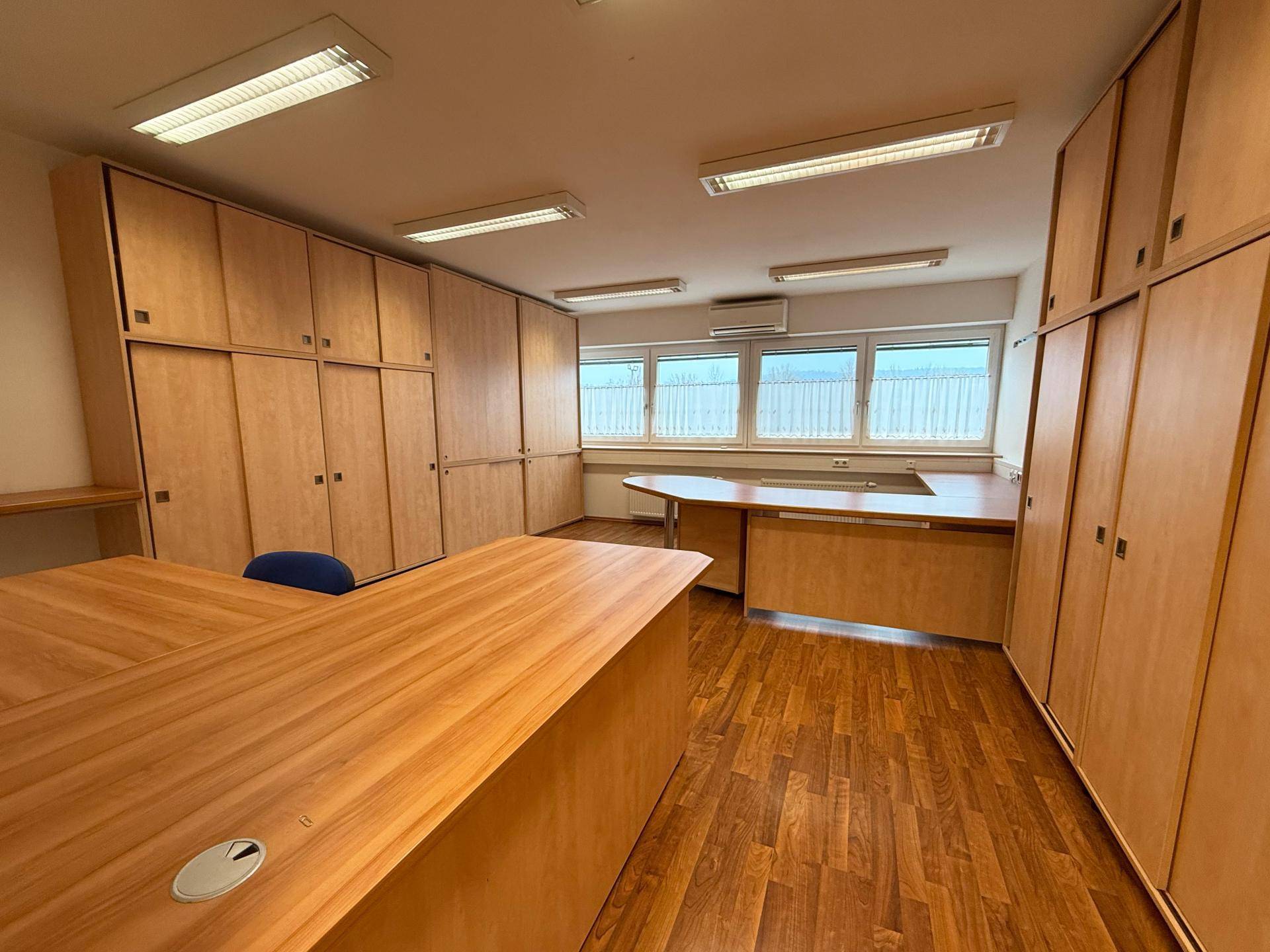 Geräumiges Büro mit vielen Holzschränken, großen Fenstern und einem großen Schreibtisch, bietet viel Stauraum.