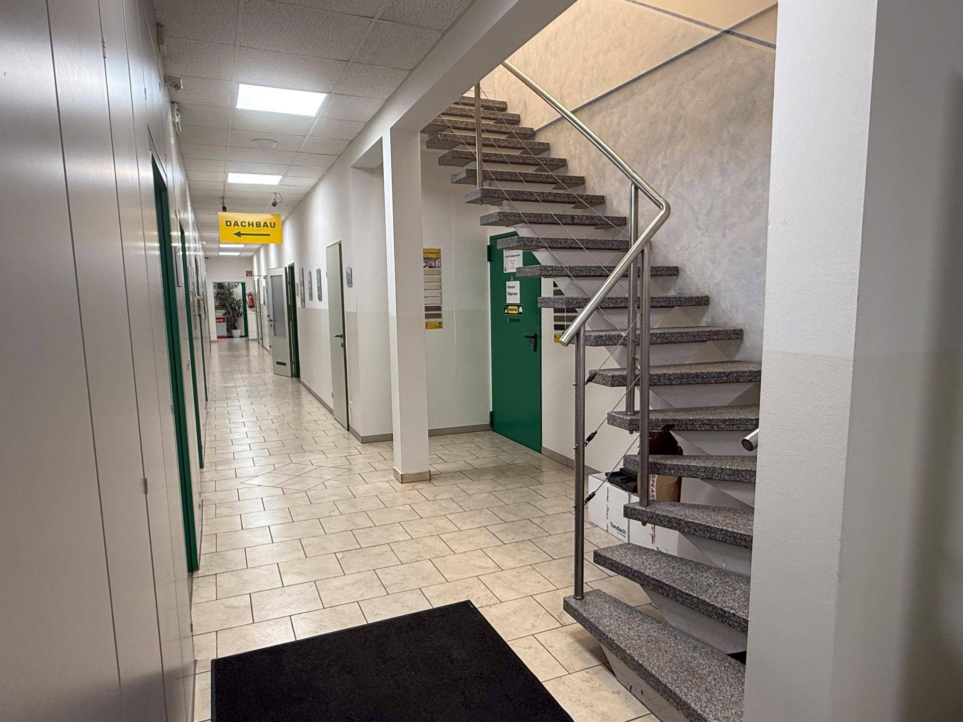 Heller Flur mit gefliestem Boden und einer modernen Treppe mit Edelstahlgeländer, verbindet verschiedene Bereiche.
