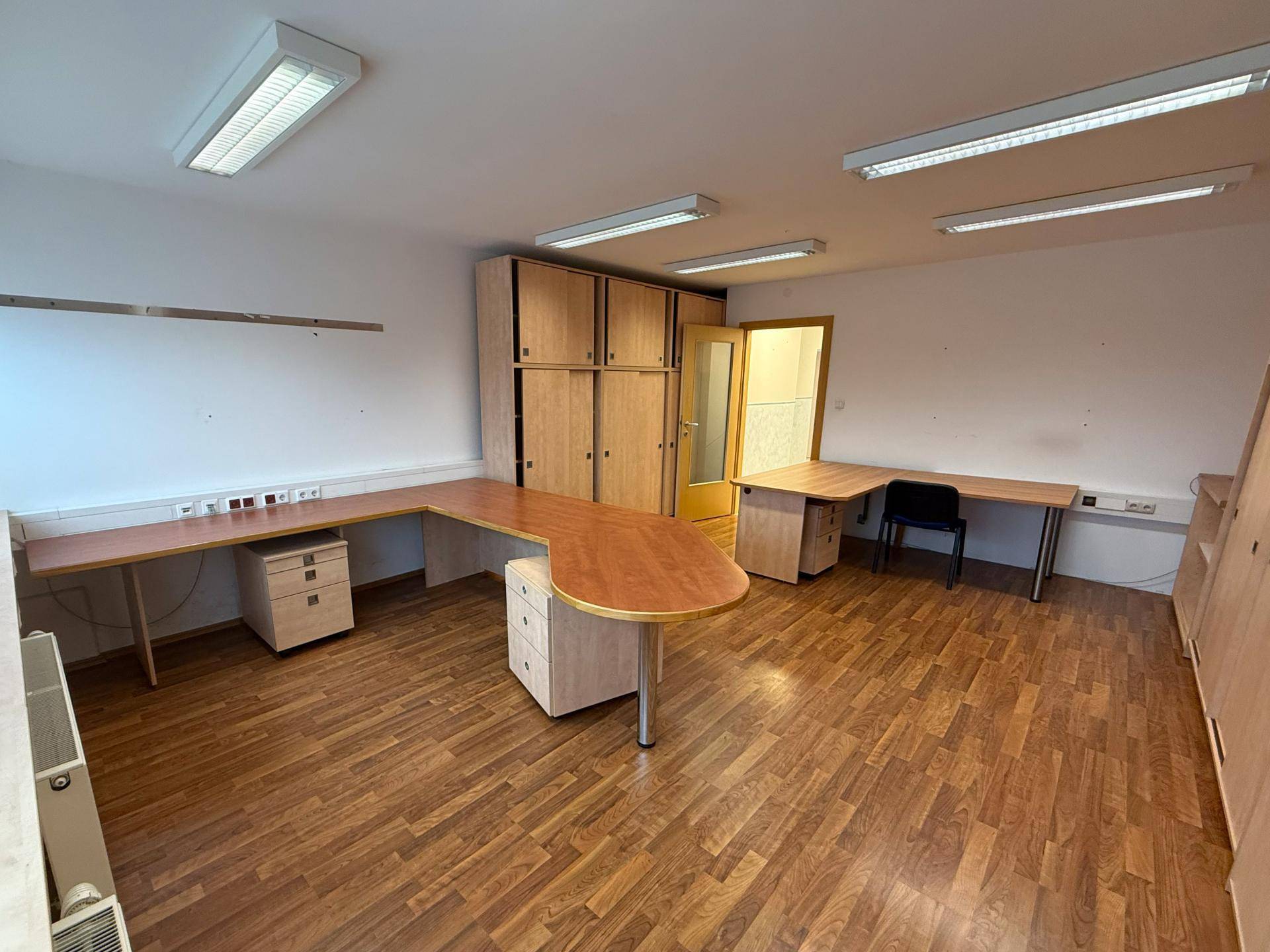 Helles Büro mit mehreren Holzschreibtischen und integrierten Schränken, bietet flexible Arbeitsplatzlösungen.