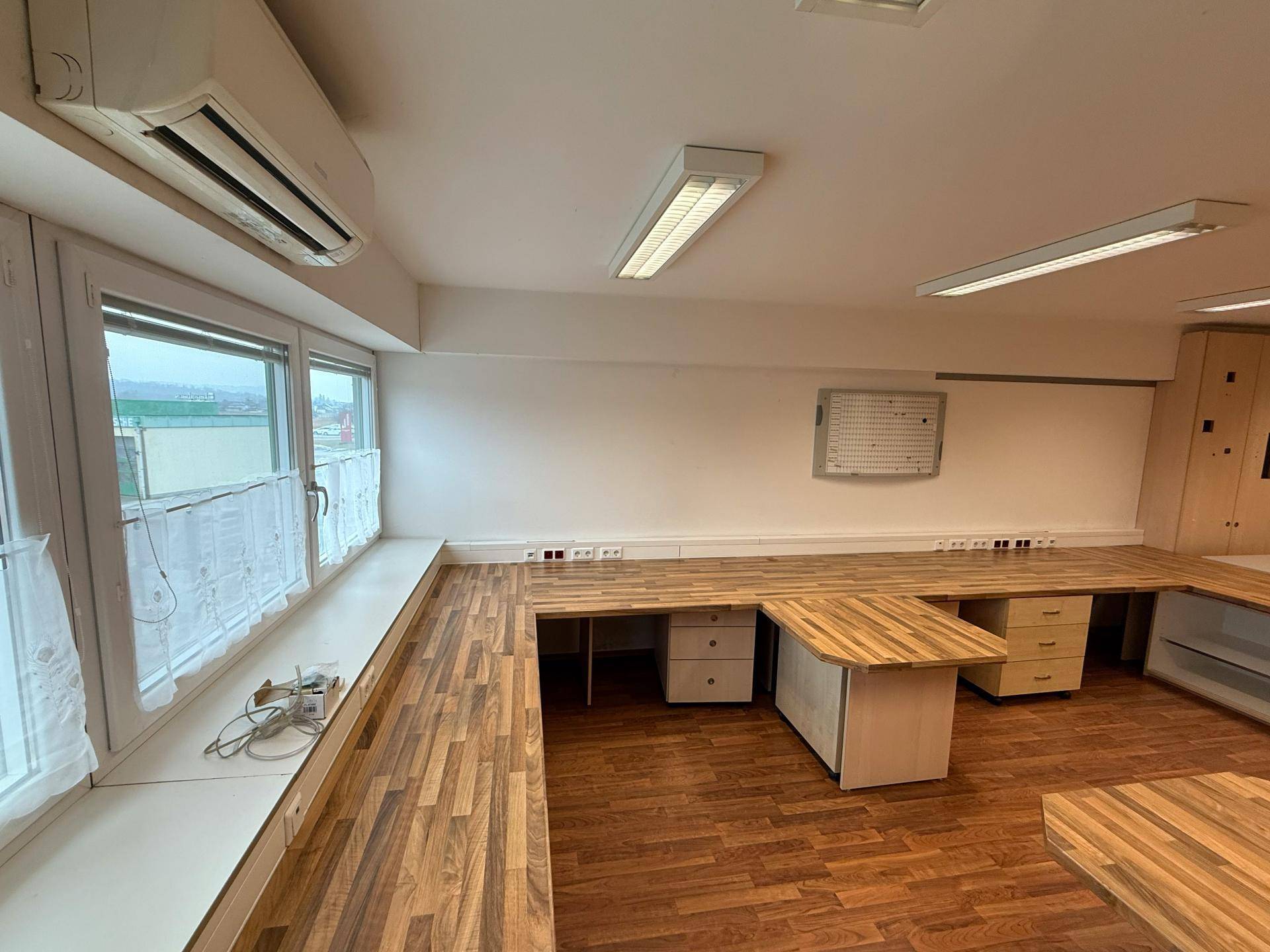 Helles Büro mit langen Arbeitsflächen entlang der Fensterfront und Klimaanlage, bietet viel Tageslicht.