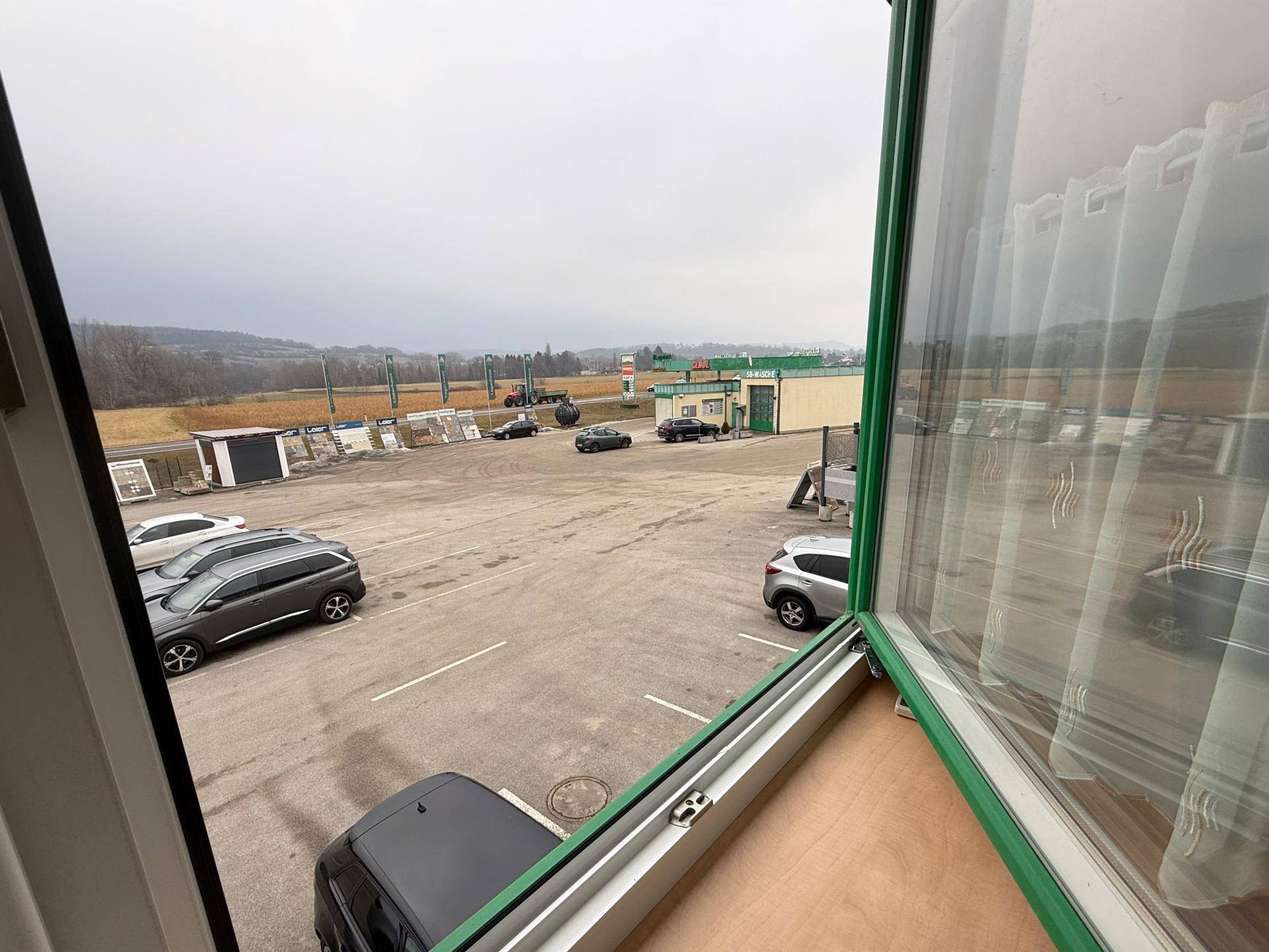 Blick aus dem Fenster auf einen großen Parkplatz und die umliegende ländliche Landschaft unter bewölktem Himmel.