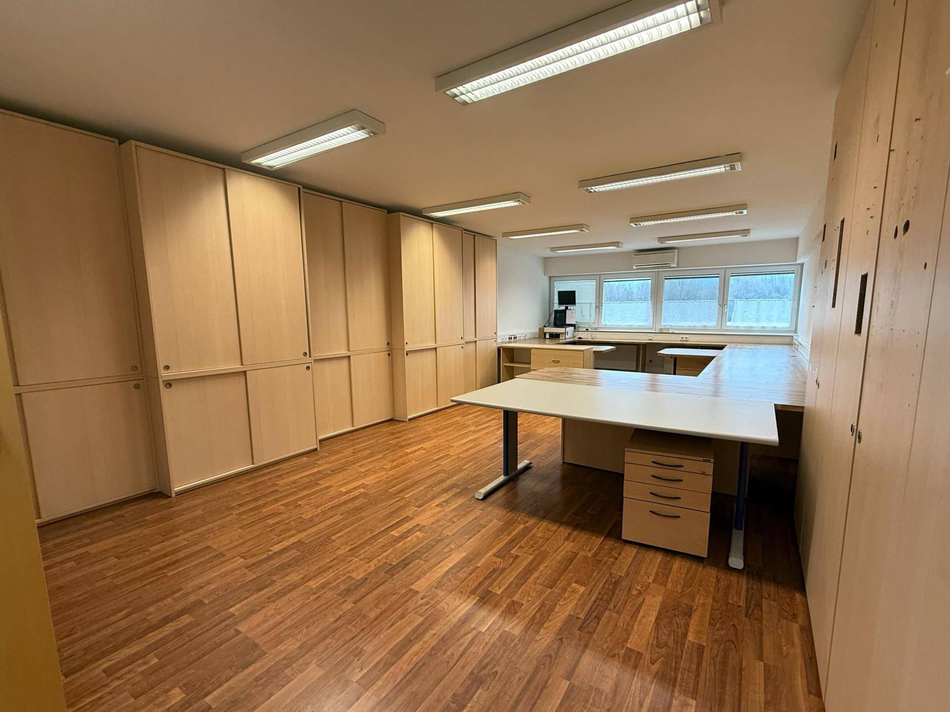 Geräumiges Büro mit vielen Holzschränken und flexiblen Arbeitsplätzen, gut beleuchtet und funktional gestaltet.