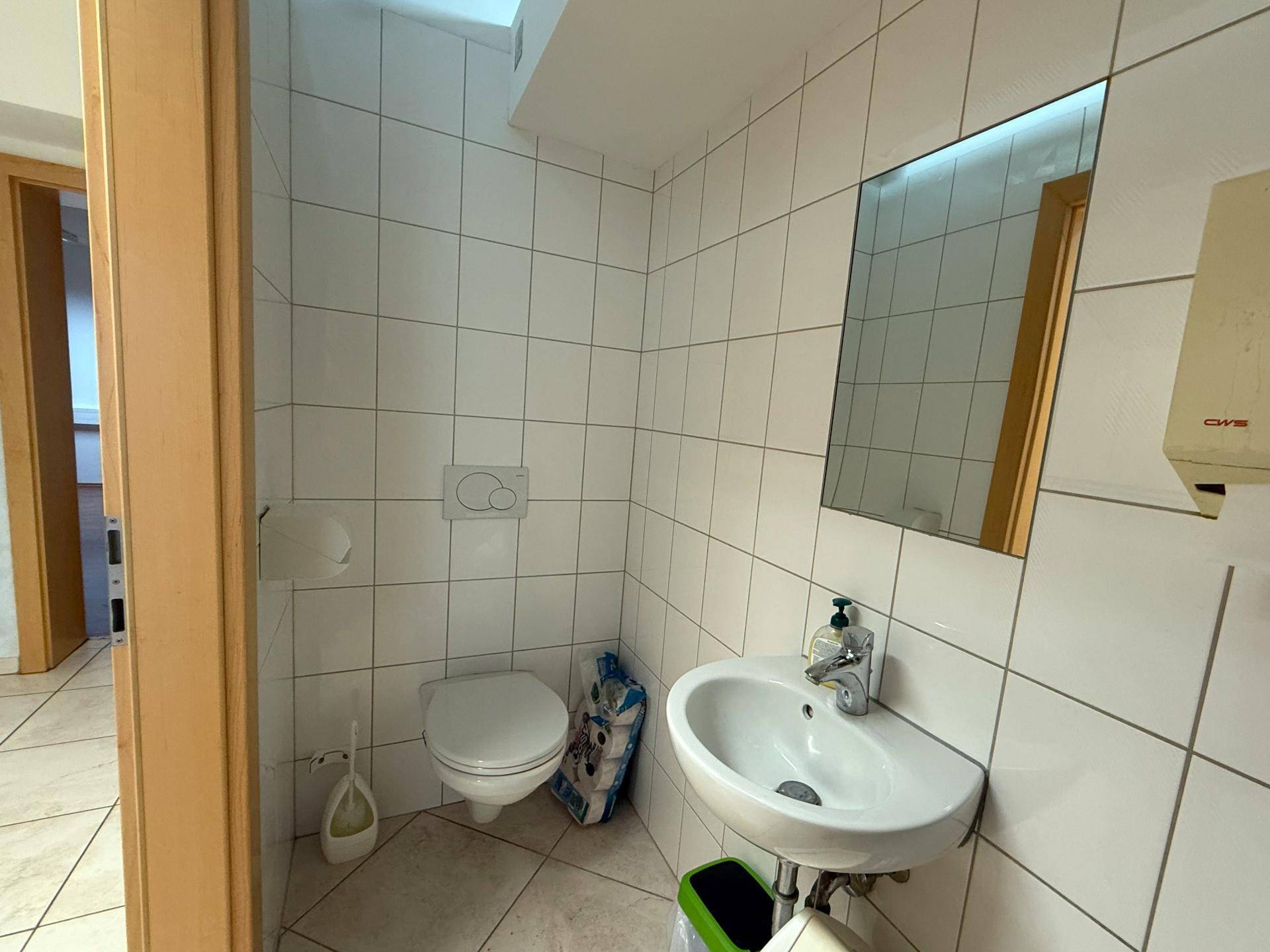 Kleiner, gefliester Toilettenraum mit Waschbecken und Spiegel, sauber und funktional gestaltet.