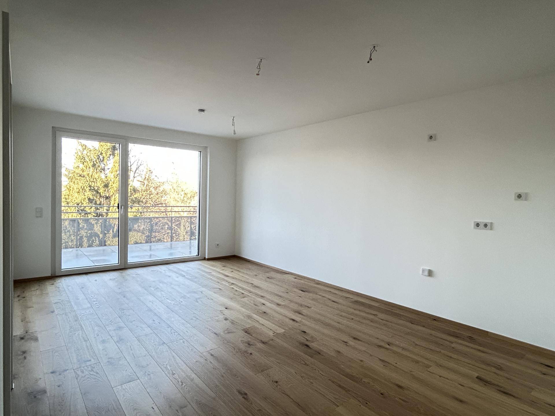 Helles Zimmer mit großem Fenster und Zugang zu einem Balkon, bietet viel Tageslicht und eine grüne Aussicht.