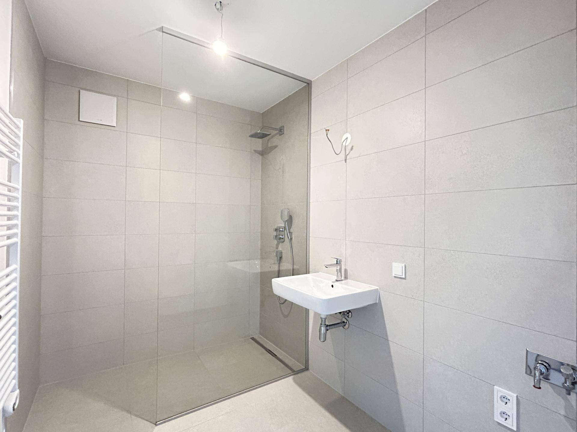 Modernes Badezimmer mit großer begehbarer Dusche, Wandfliesen in Grautönen und einem Heizkörper.