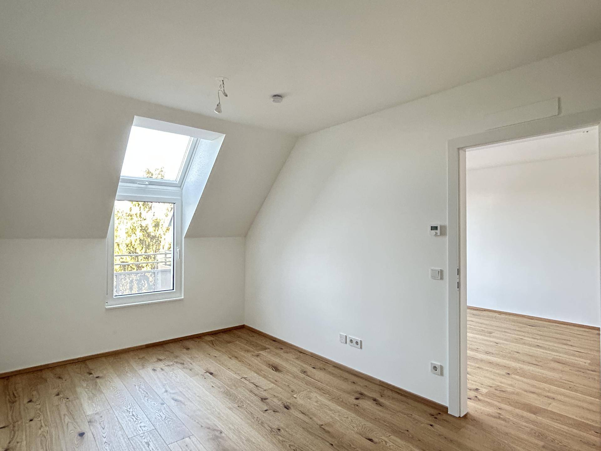 Gemütliches Zimmer im Dachgeschoss mit schrägen Wänden, Dachfenster und hellem Holzfußboden.