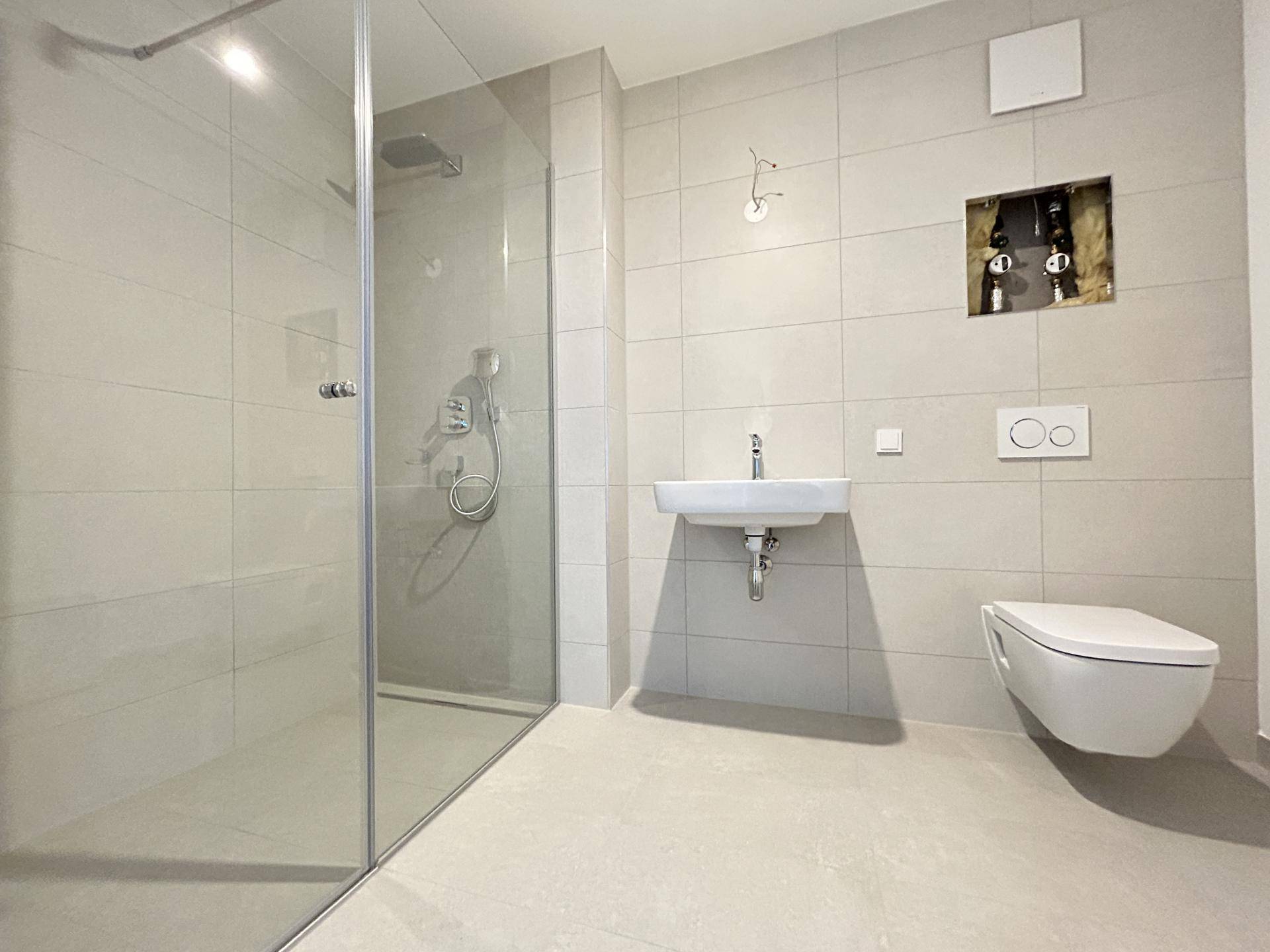 Modernes Badezimmer mit hellgrauen Fliesen, begehbarer Dusche und wandhängendem WC.