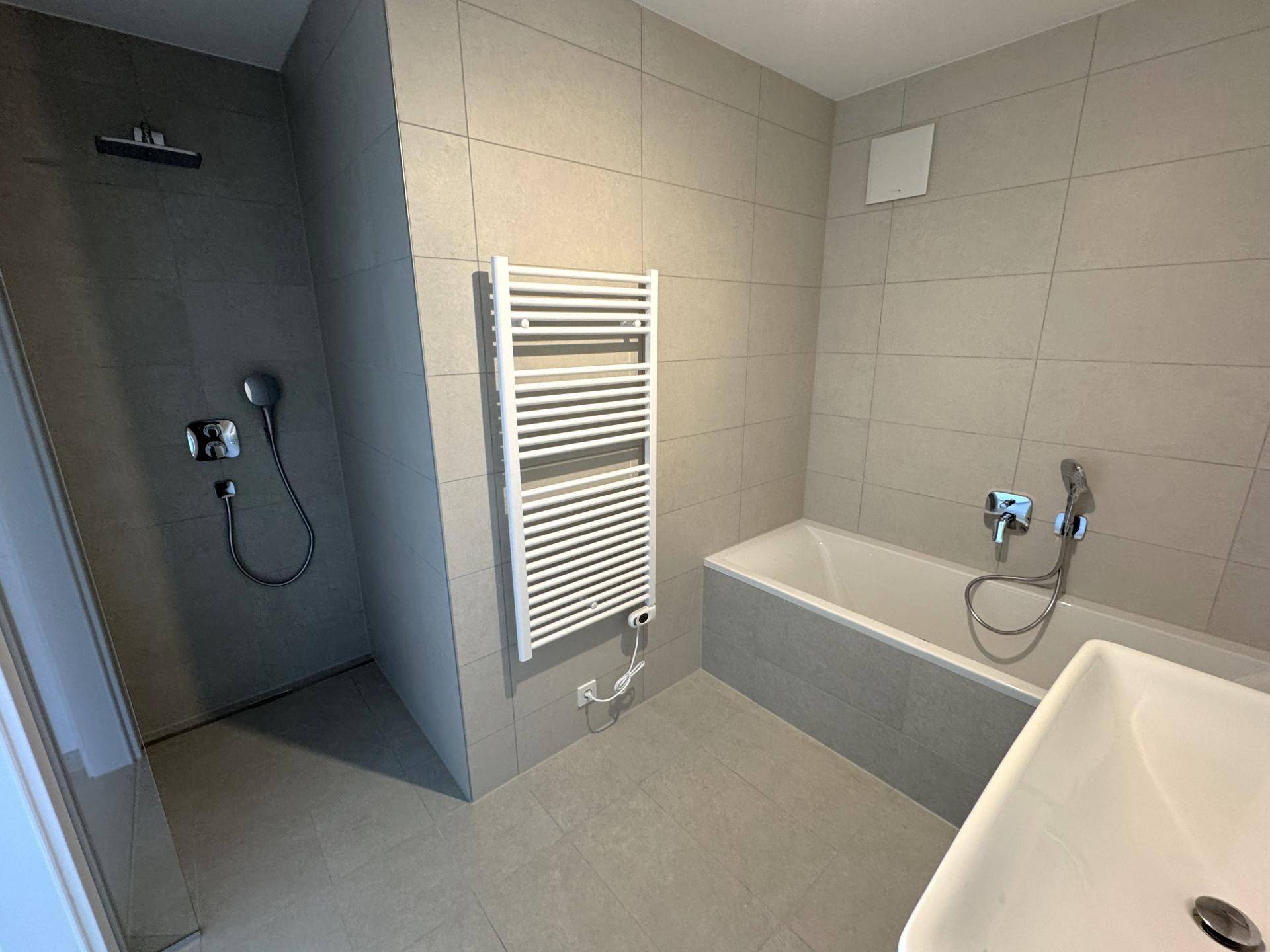 Modernes Badezimmer mit grauen Fliesen, Badewanne, Dusche und beheiztem Handtuchhalter.
