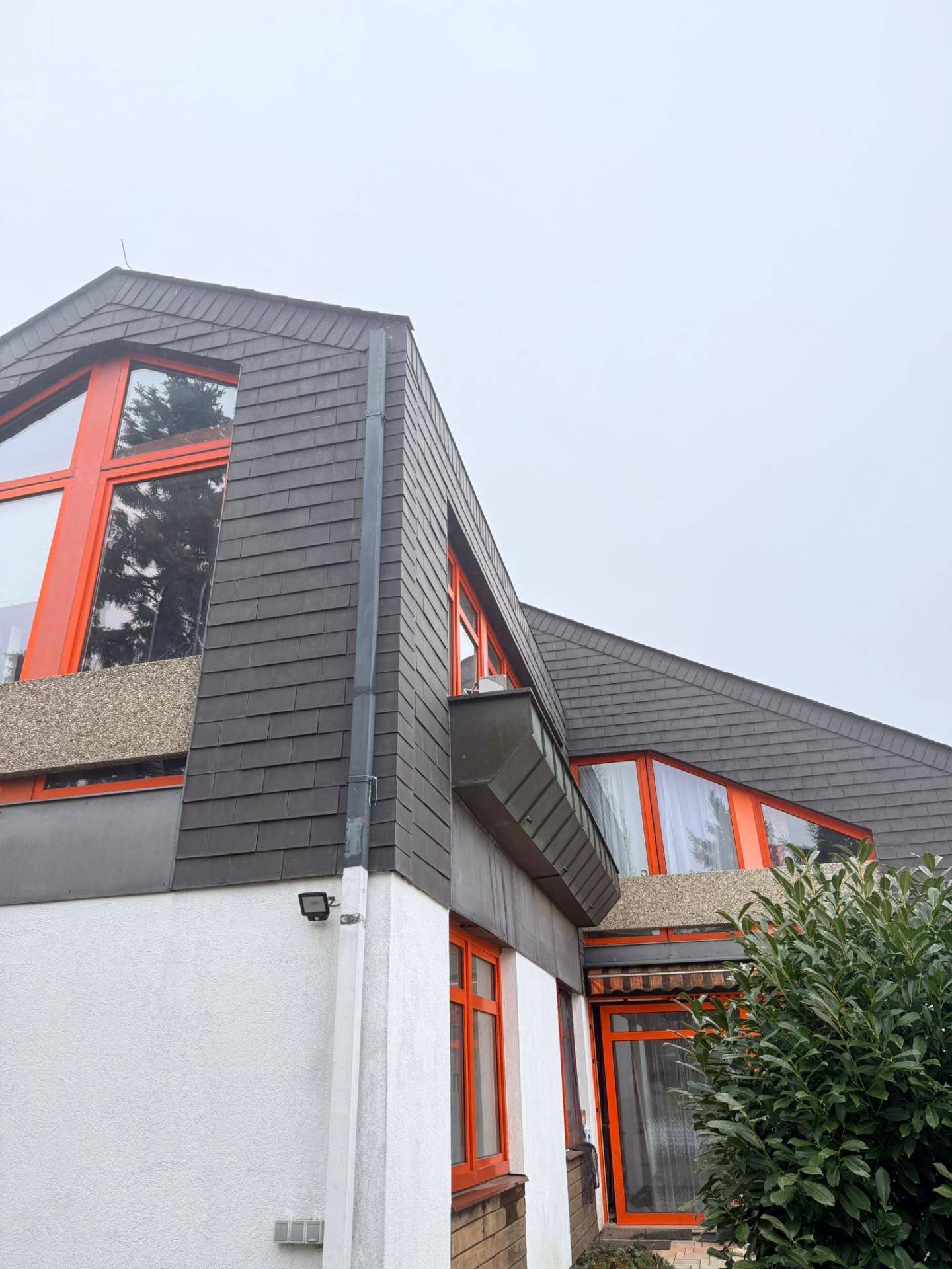 Detailansicht der Hausfassade mit Schieferdach und auffälligen orangefarbenen Fensterrahmen.