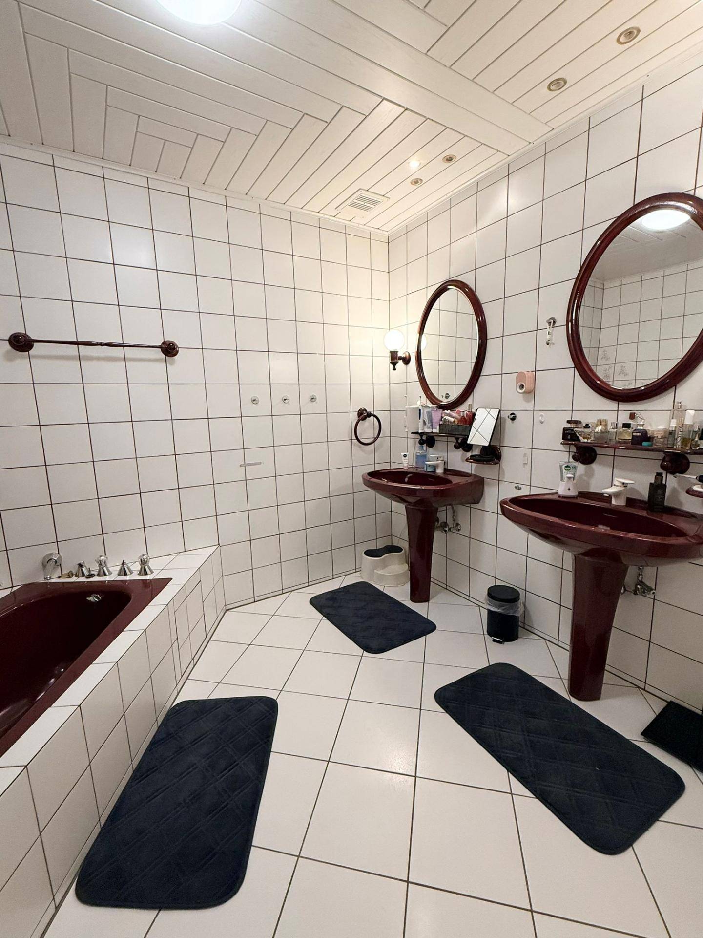 Badezimmer mit weißen Fliesen, zwei Waschbecken und einer eingebauten Badewanne in Rotbraun.