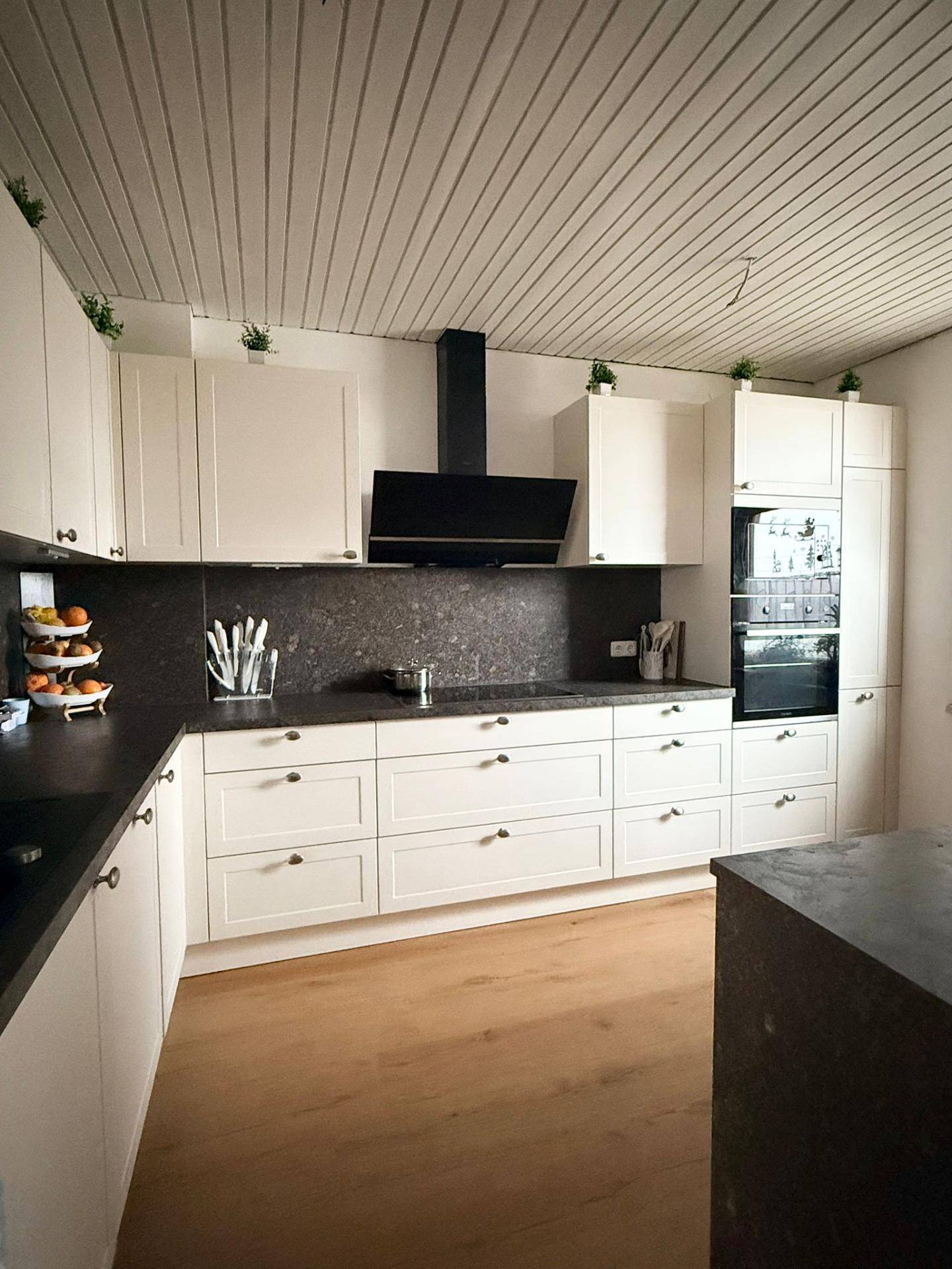 Moderne Küche mit weißen Schränken, dunkler Arbeitsplatte und Holzboden.