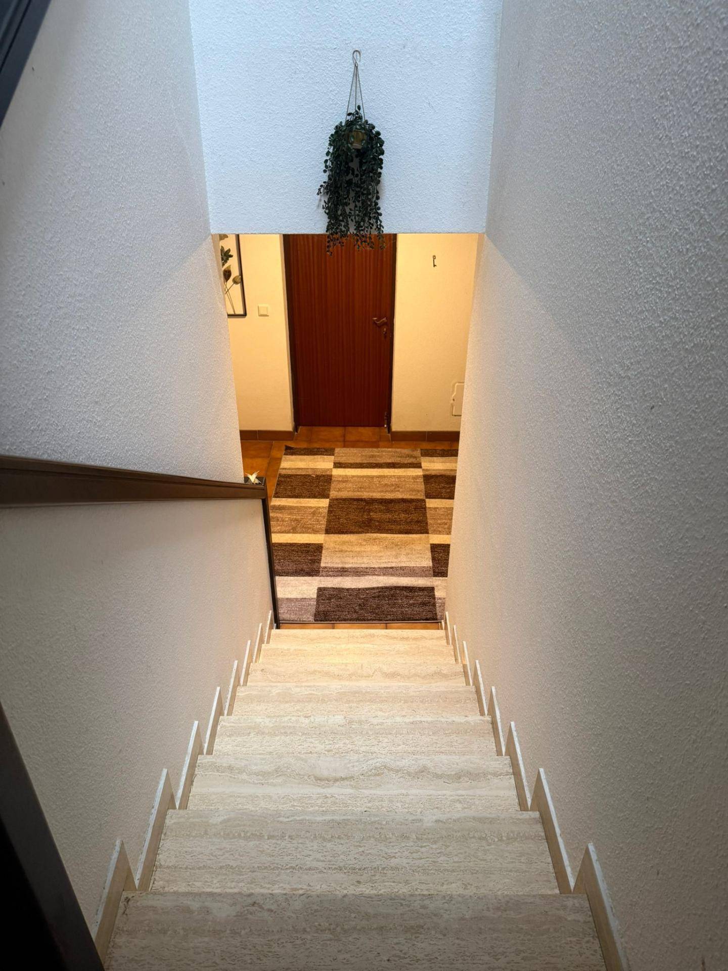Blick vom oberen Treppenabsatz auf die Steintreppe und den Flur mit gemustertem Teppich.