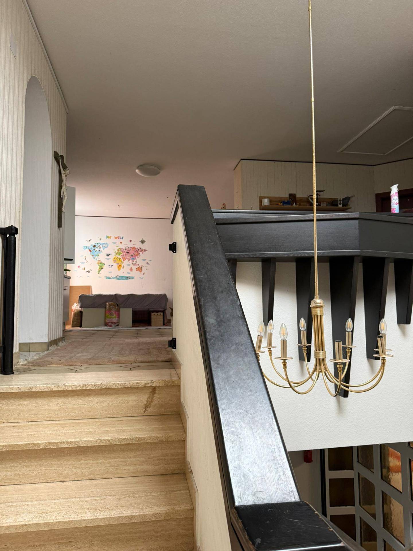 Treppenhaus mit Holzgeländer und einem Kronleuchter, der zu einem oberen Bereich führt.