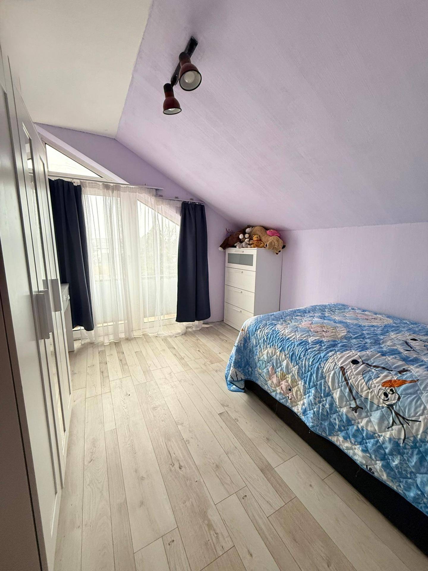 Helles Schlafzimmer im Dachgeschoss mit schräger Decke, Laminatboden und großem Fenster.