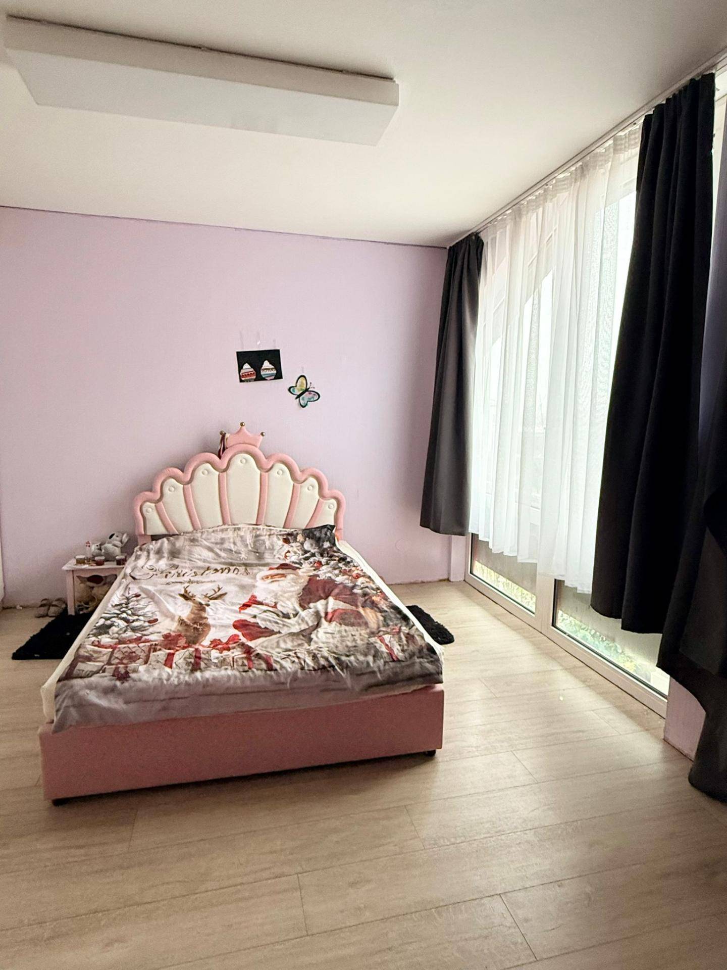 Kinderzimmer mit rosa Wänden, Laminatboden und großen Fenstern, die viel Licht hereinlassen.